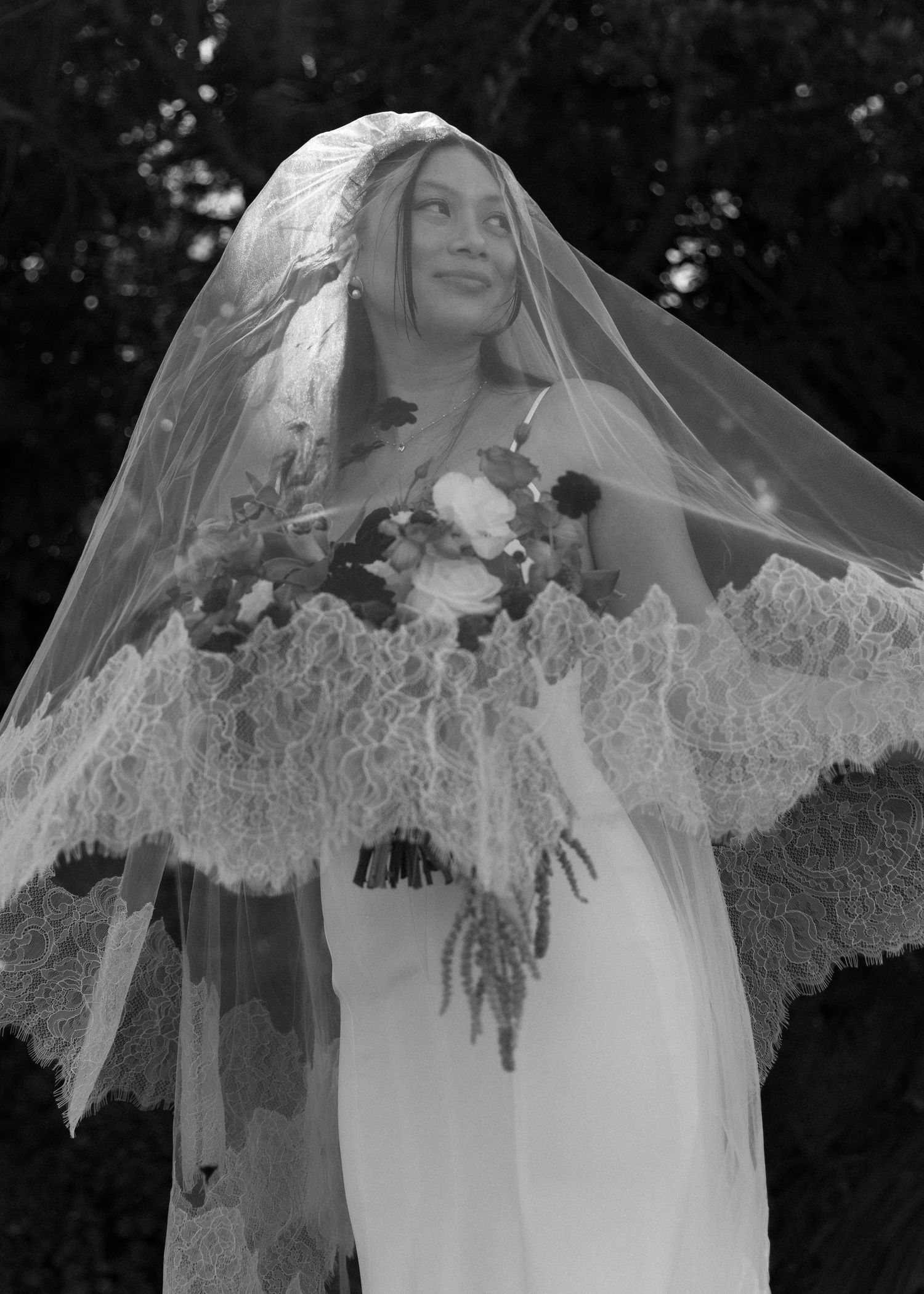 Elegant bride wearing a flowing lace veil against a dark background.