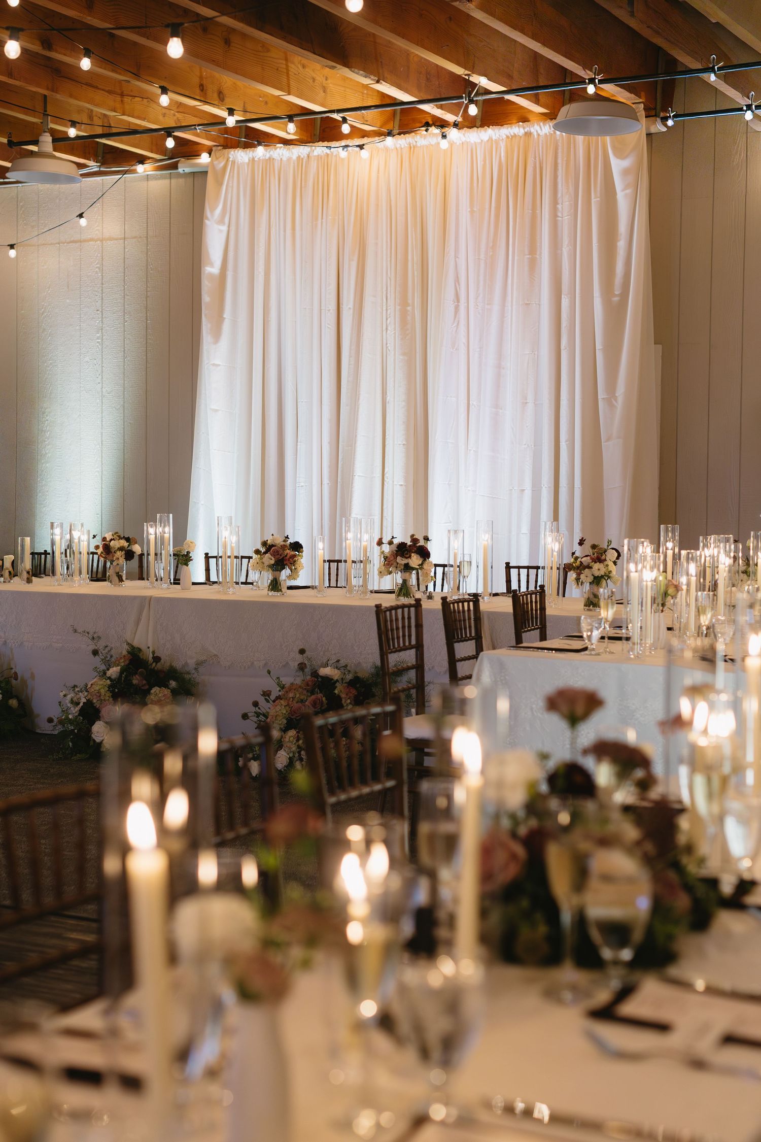 Elegant wedding reception setup with white draping, string lights and candlelit tables.