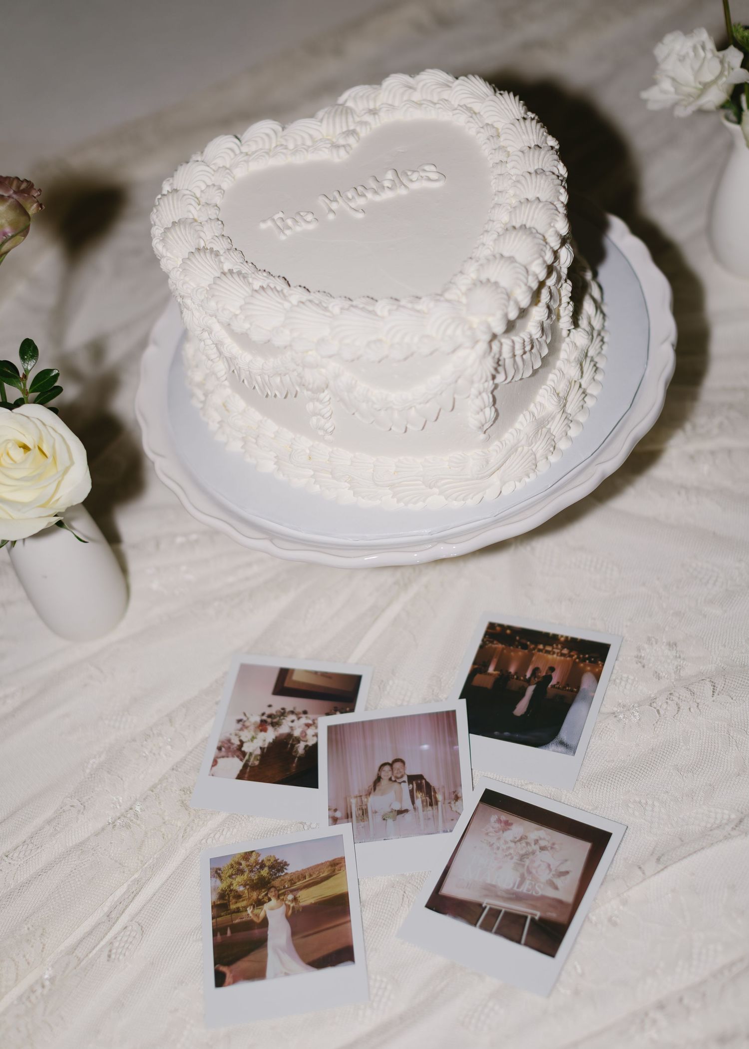 Heart-shaped white wedding cake displayed with vintage photographs on white tablecloth.
