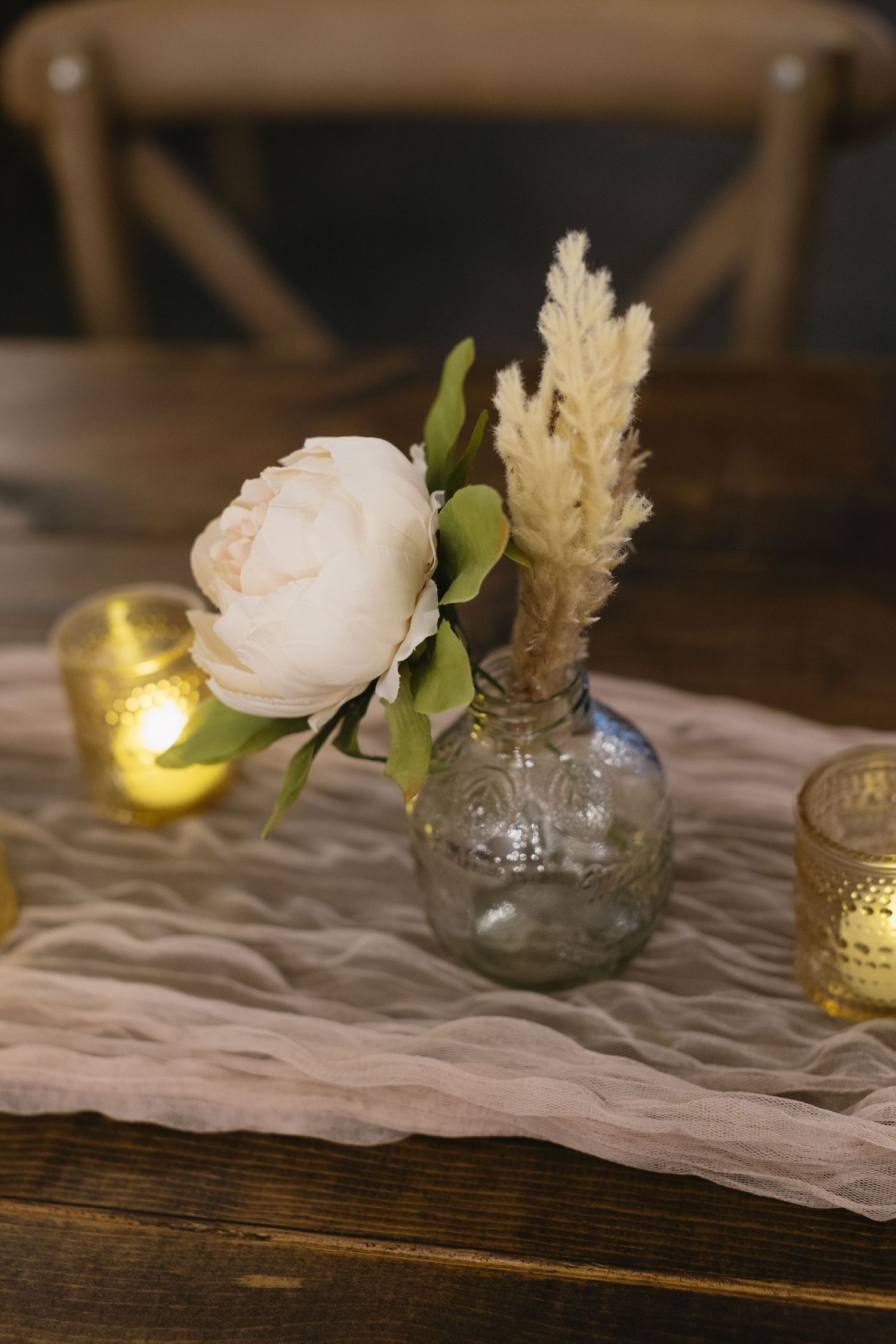 White peony flower arrangement with pampas grass in a glass vase with candlelight.