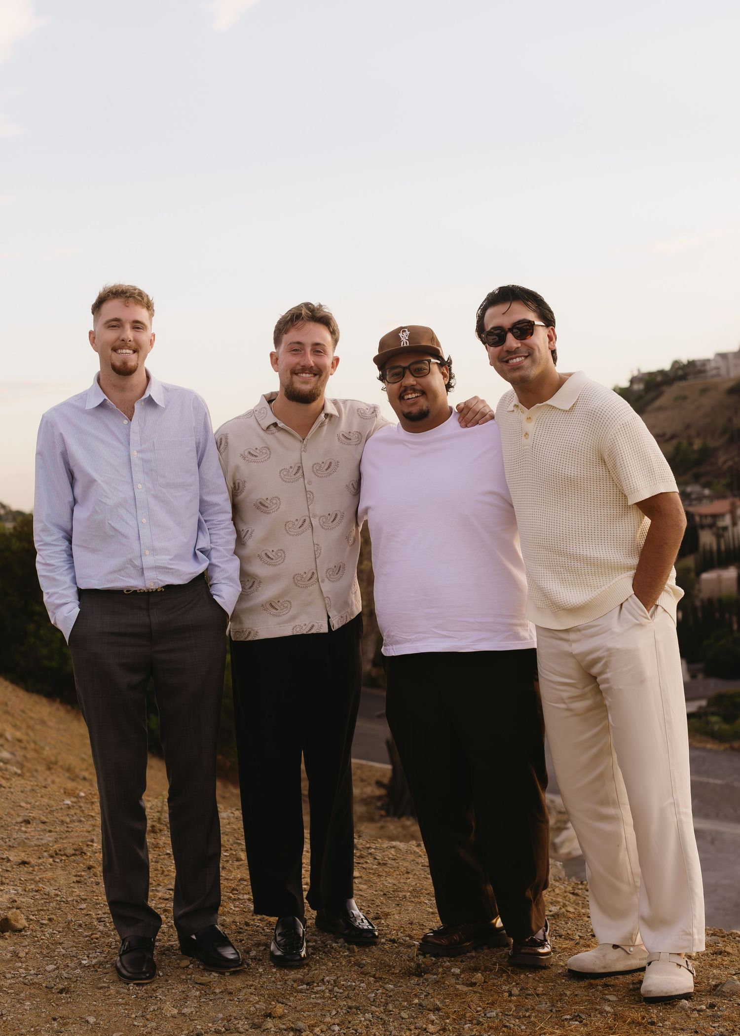 Group photo of wedding party members posing together outdoors at sunset.
