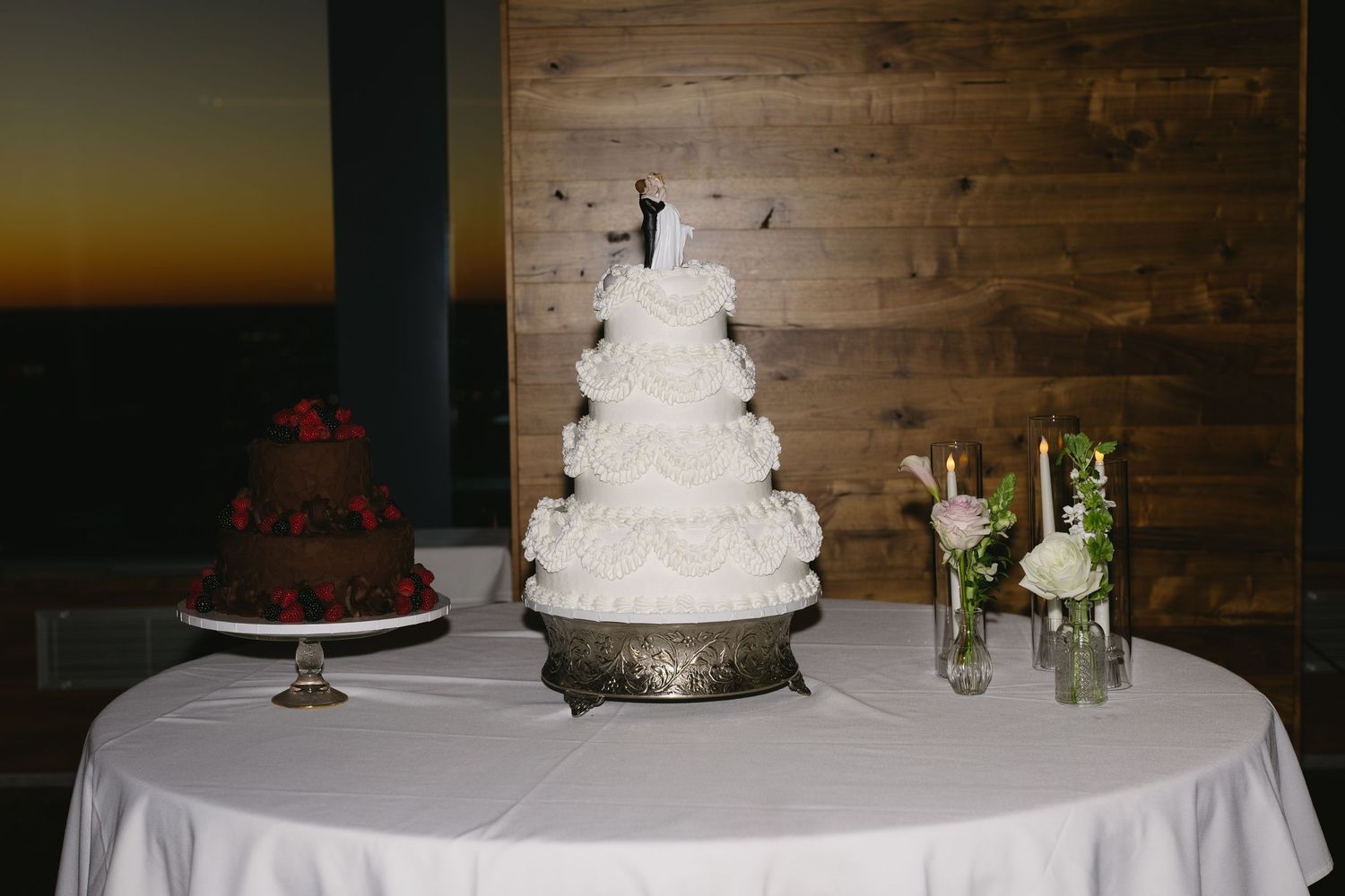 A wedding cake display table with rustic wood backdrop and white linens.
