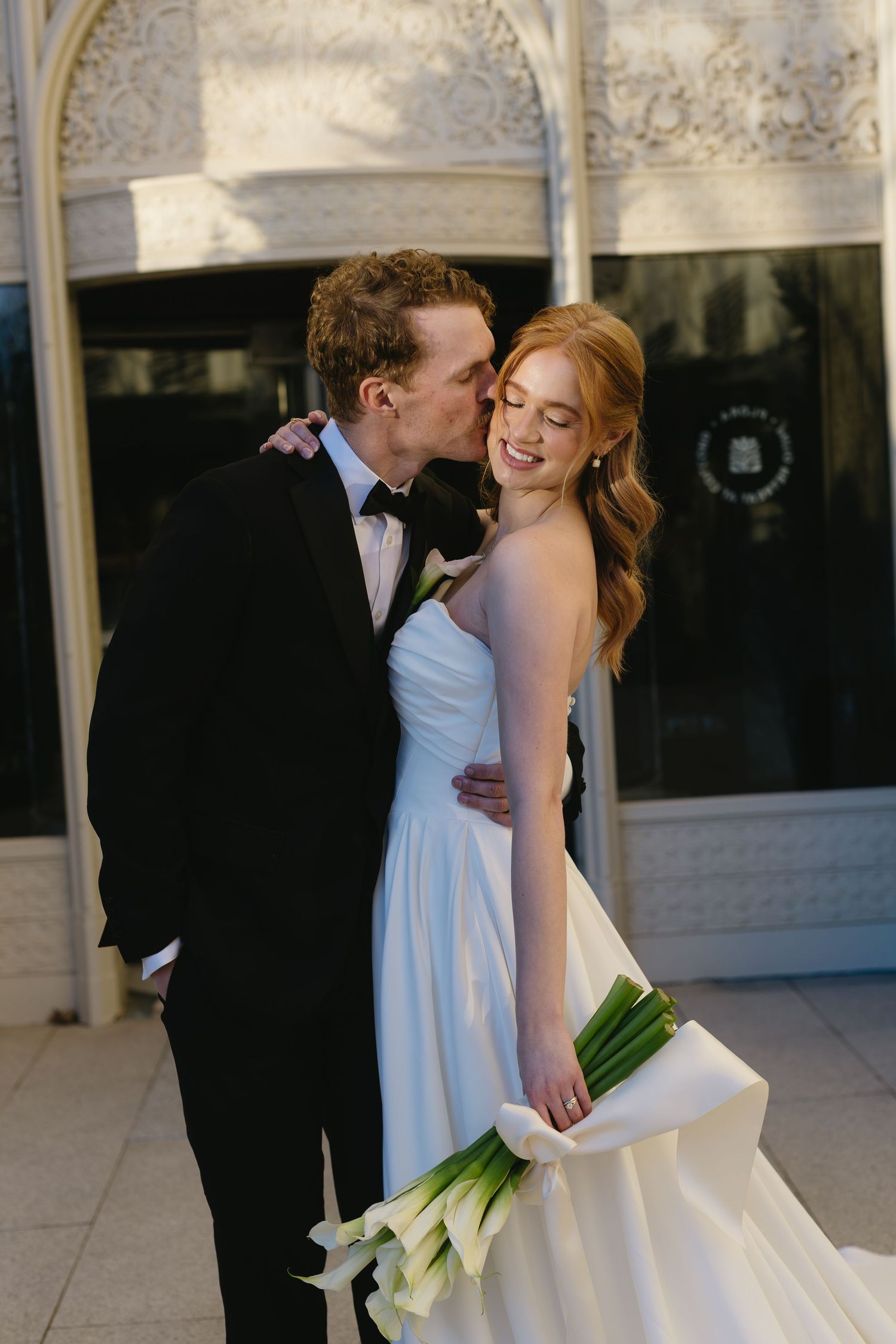 A bride in a white gown and groom in black tuxedo share an intimate moment during their wedding portraits.