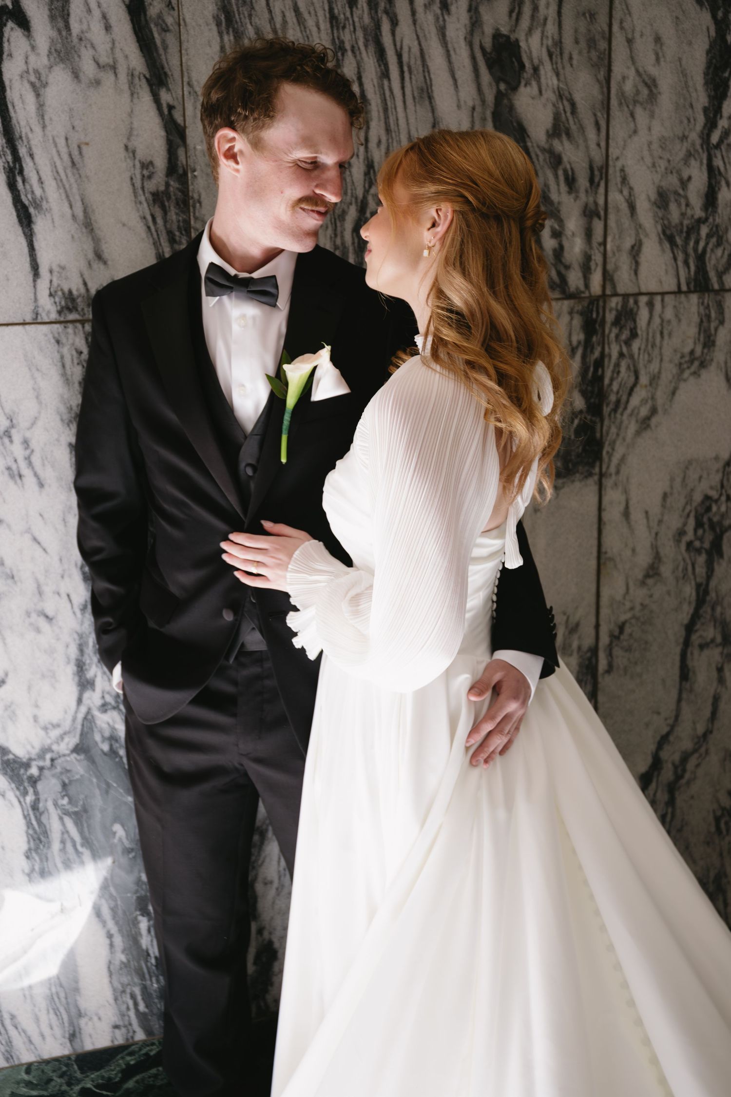 Wedding couple posing against marble walls in formal attire.