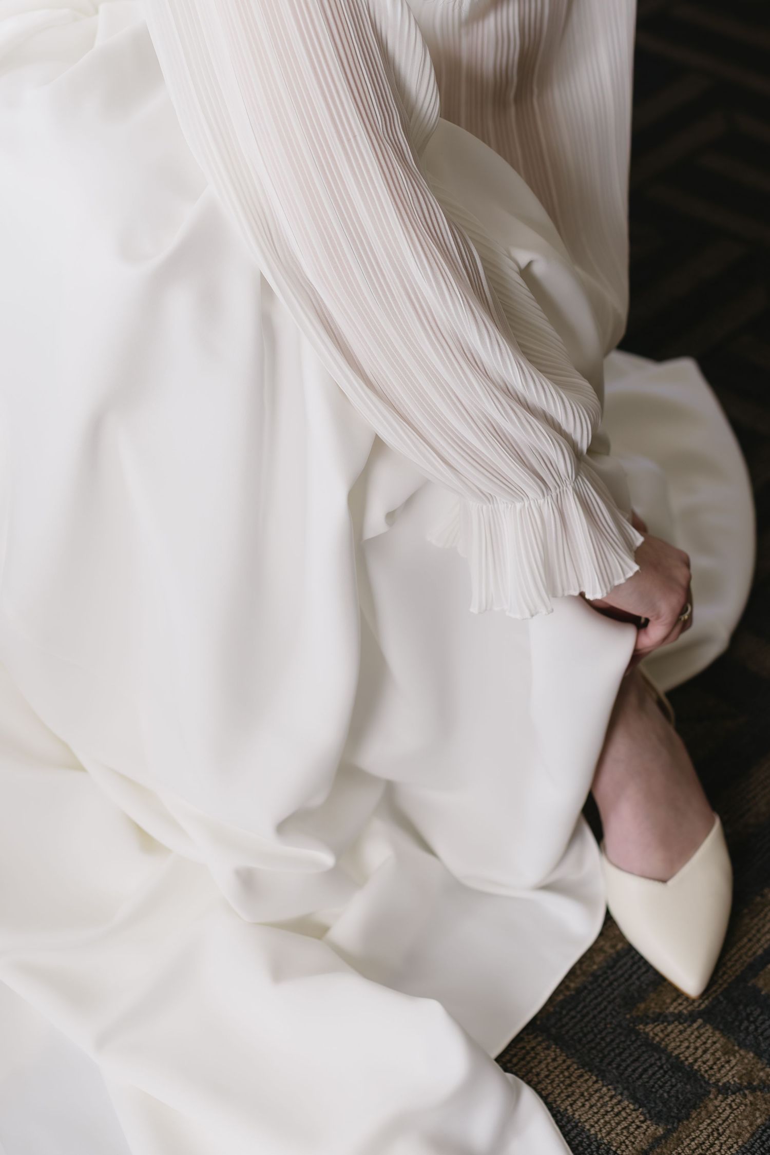 Detail shot of white bridal gown fabric against geometric patterned carpet.