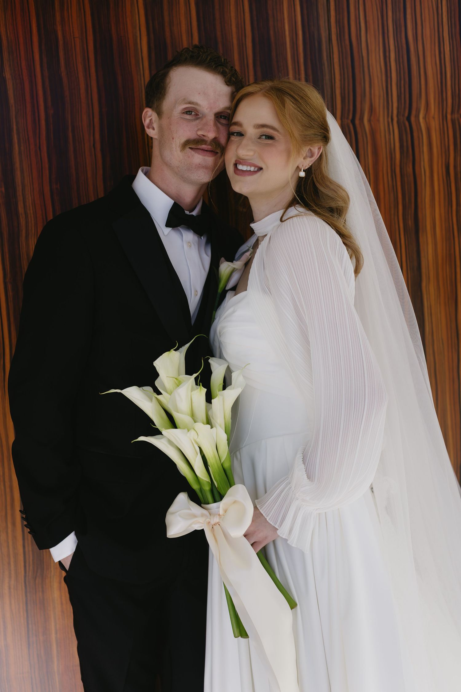 Elegant wedding portrait with calla lilies against wood paneling.