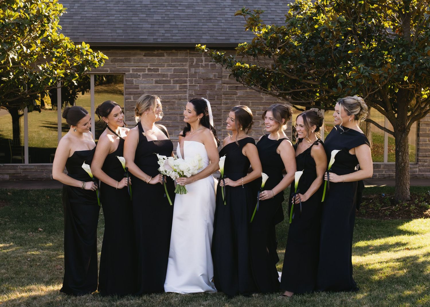 Wedding party in black and white attire photographed together on sunny lawn.