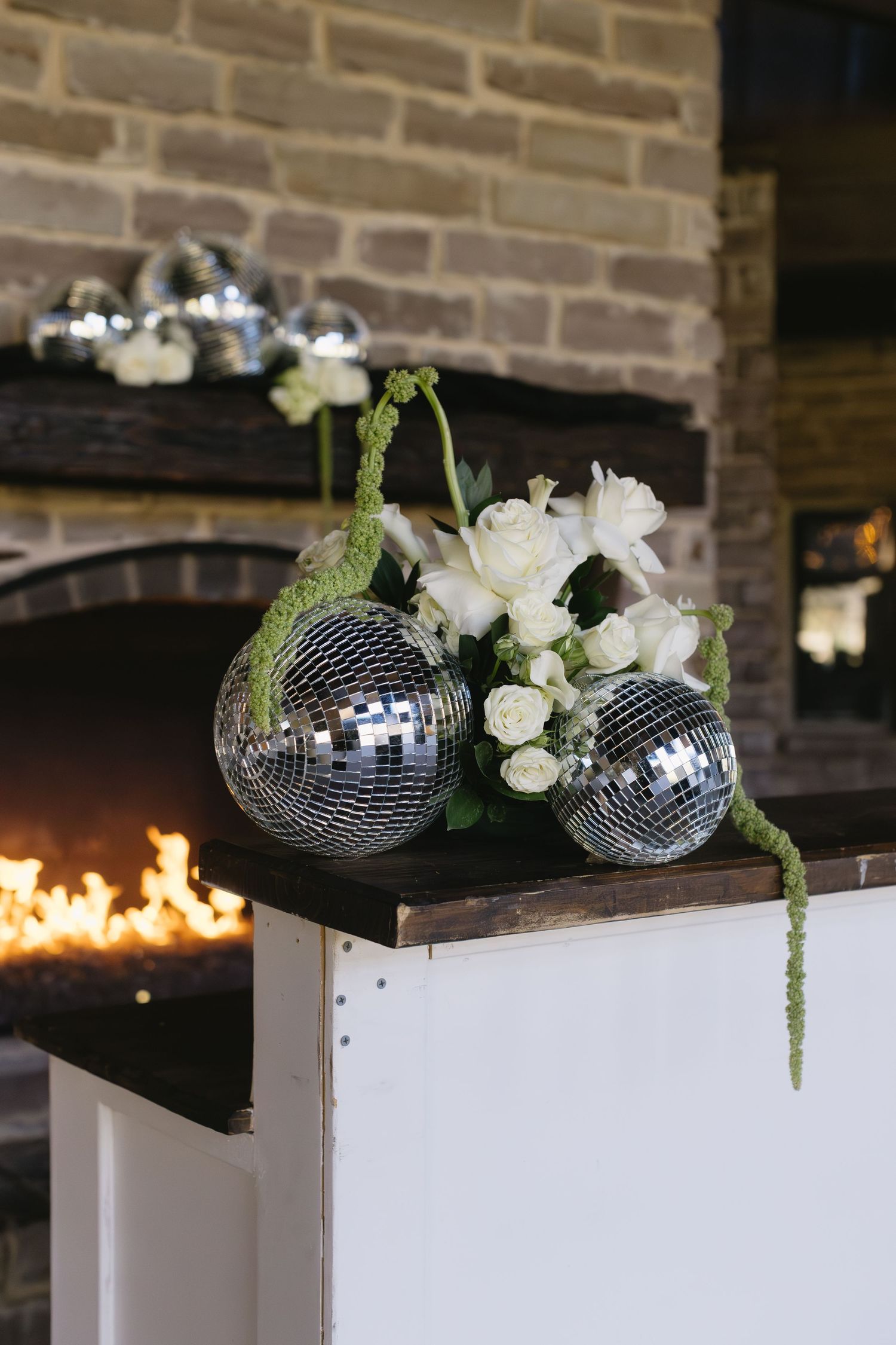 Disco balls decorated with white flowers on display near a fireplace.