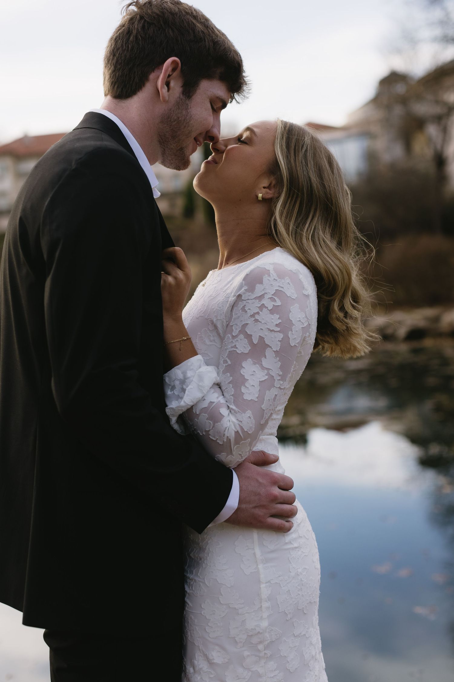 A couple shares an intimate moment by a waterfront during golden hour.