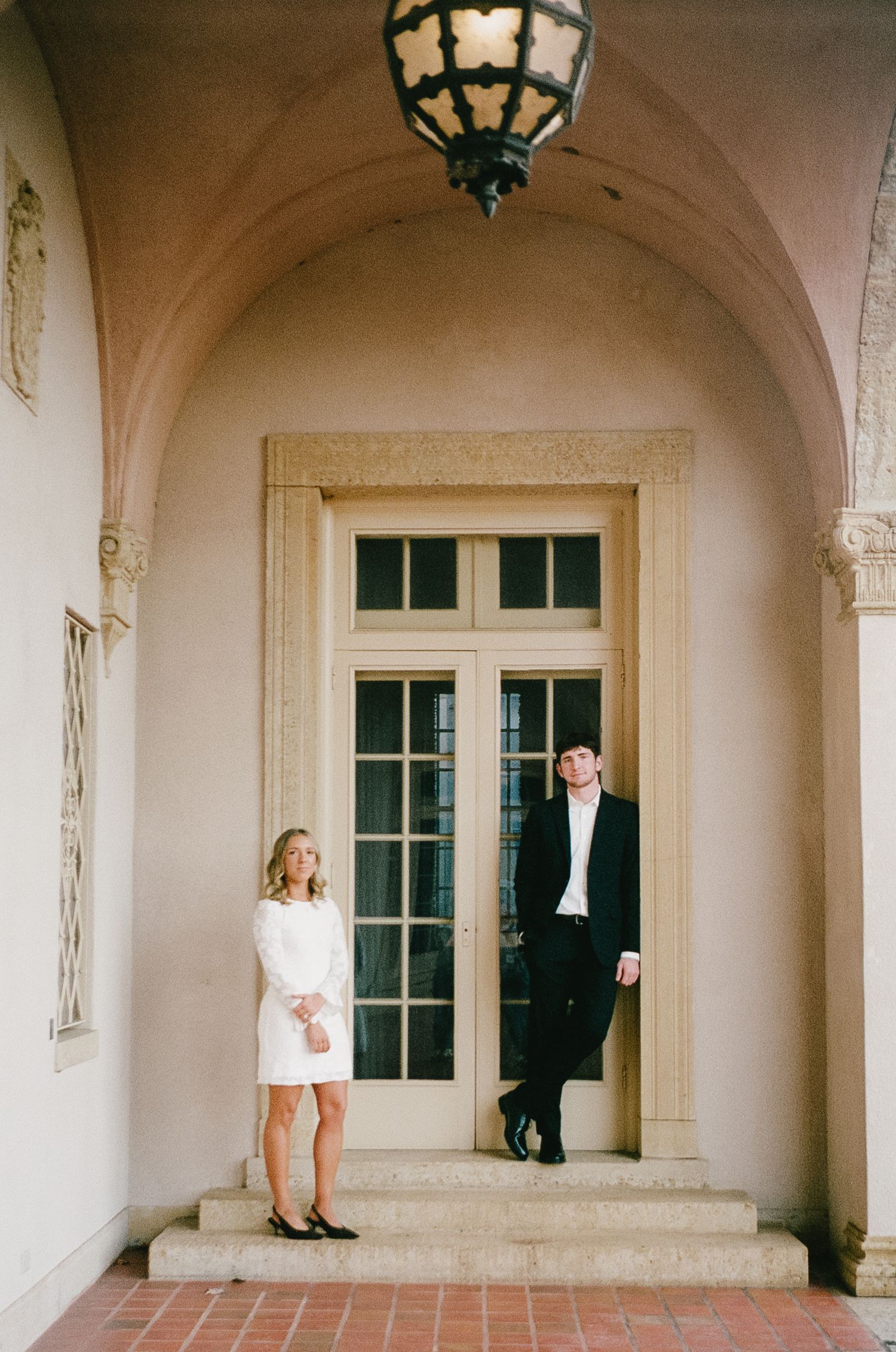 A couple poses playfully in an elegant arched colonnade with hanging lanterns.
