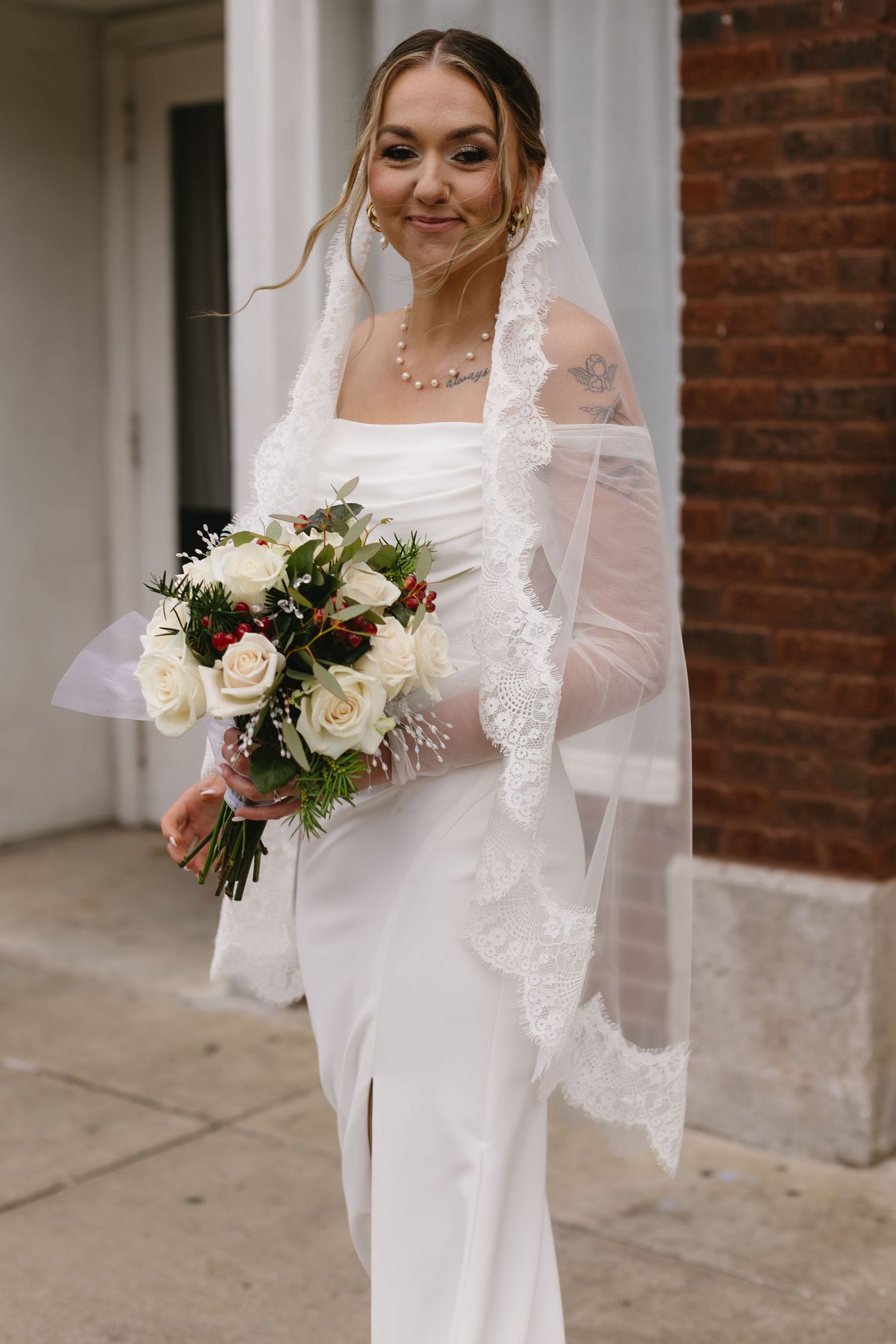Bride in elegant white gown and veil holds a winter wedding bouquet with white roses.