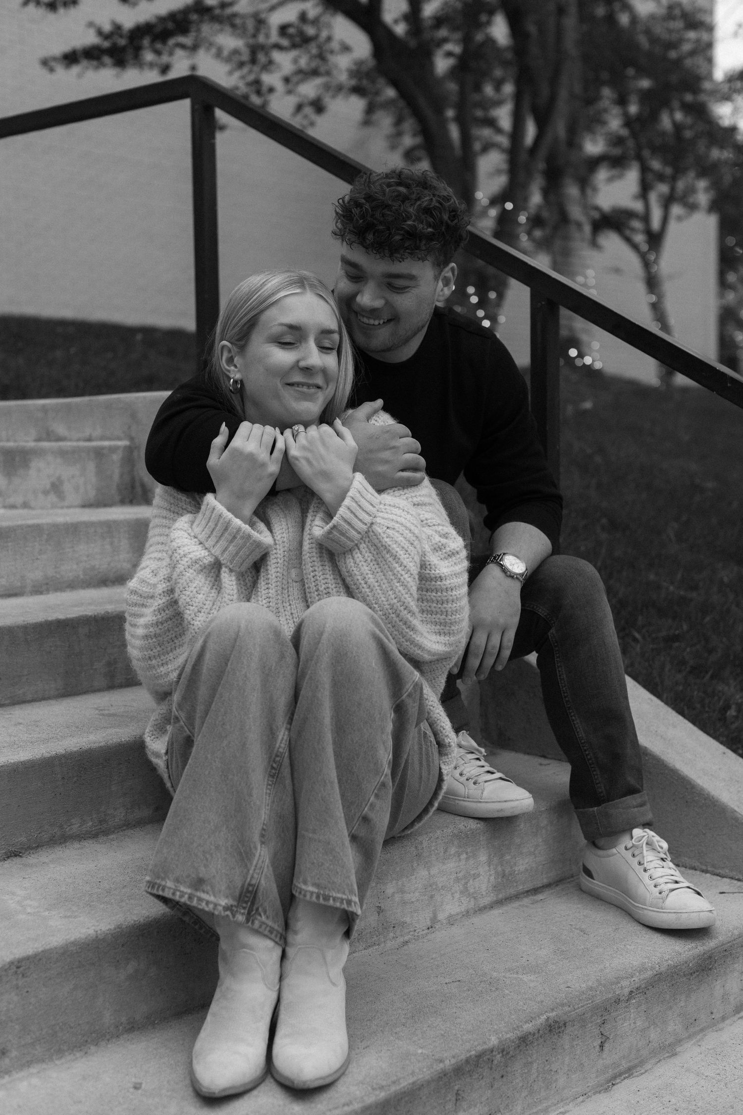A couple sitting on concrete steps outdoors, with one wearing a cozy white sweater and the other in dark clothing.