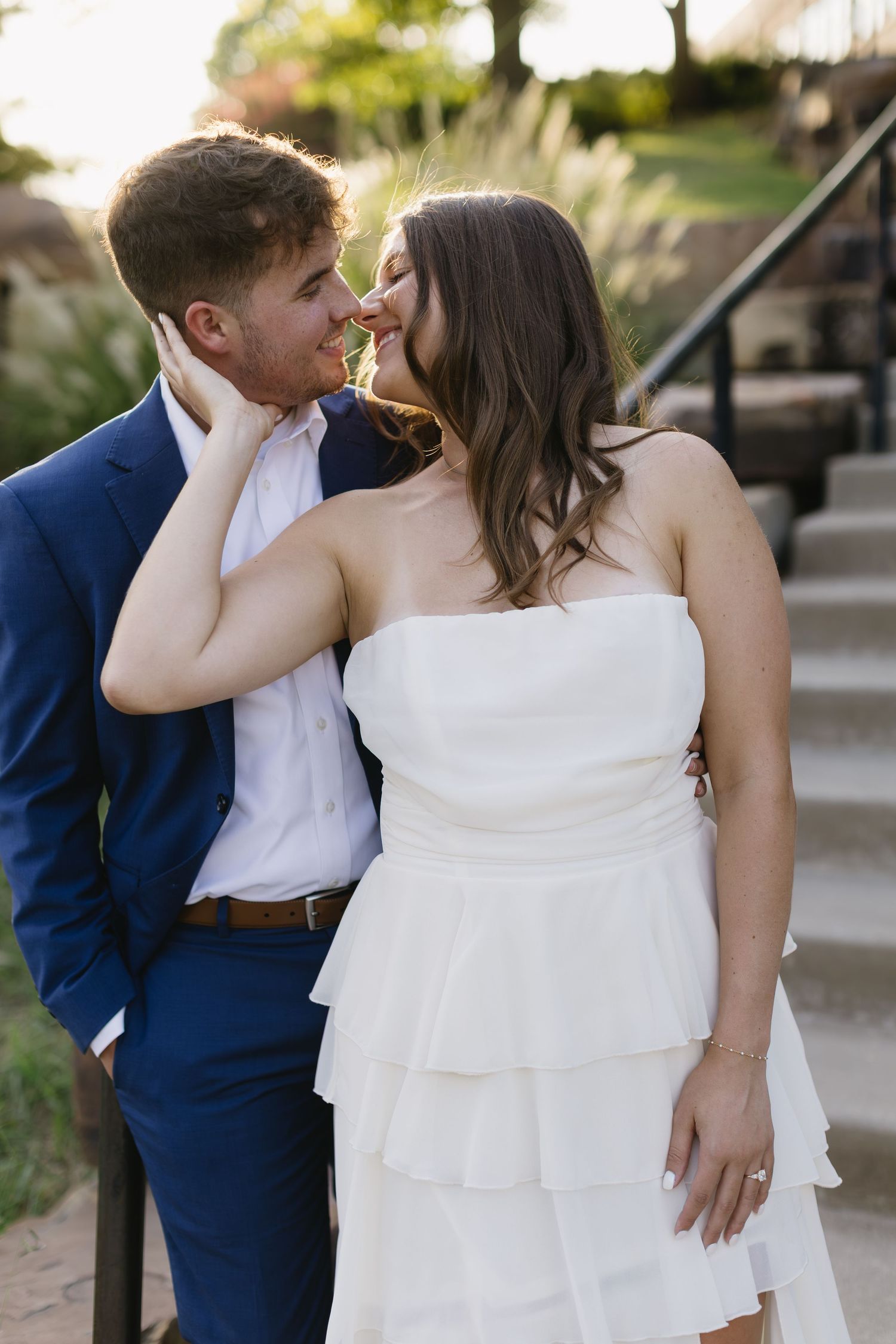 A romantic couple in wedding attire share an intimate moment on stone steps.