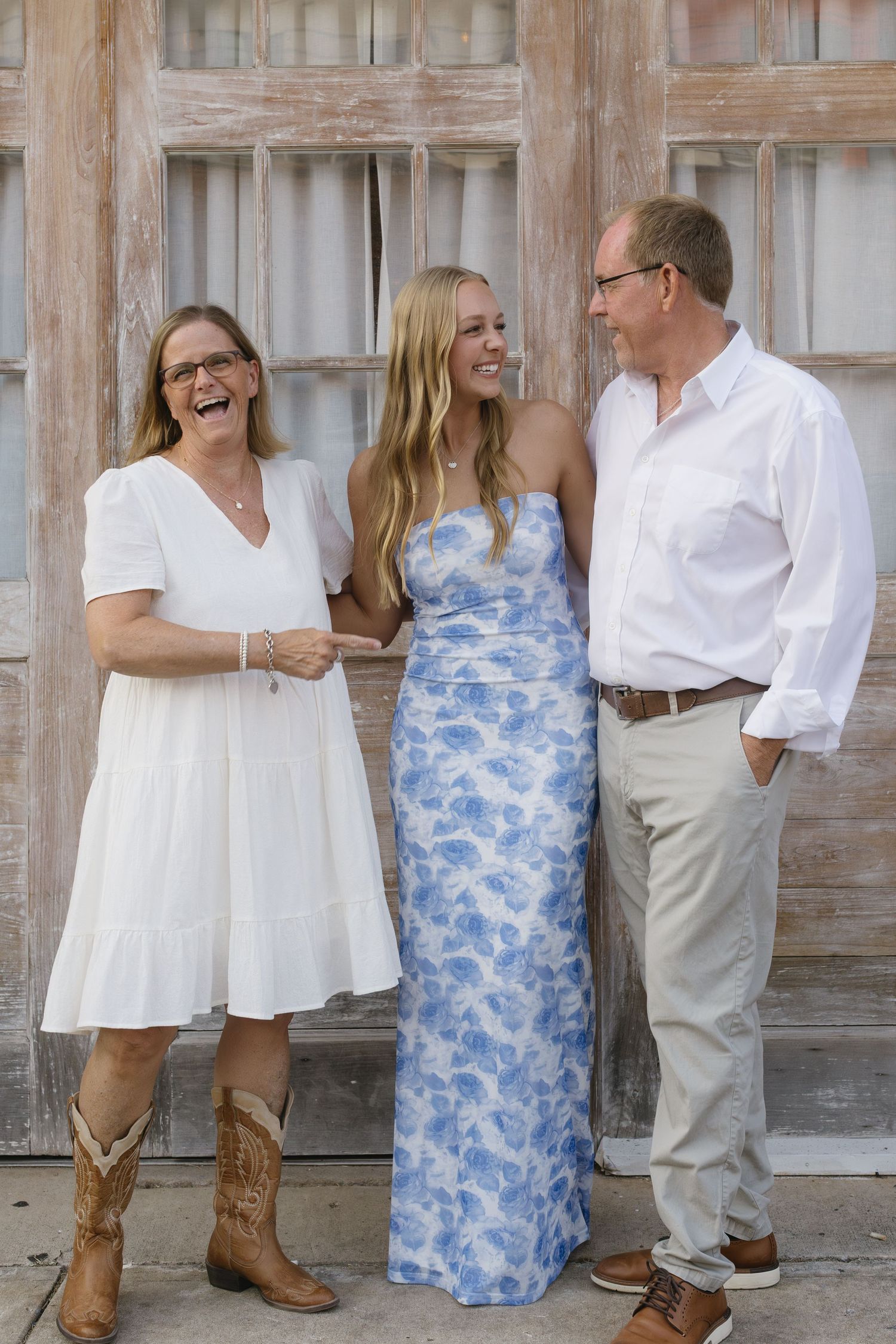 A group poses against a weathered wooden wall with some wearing white and blue floral attire.