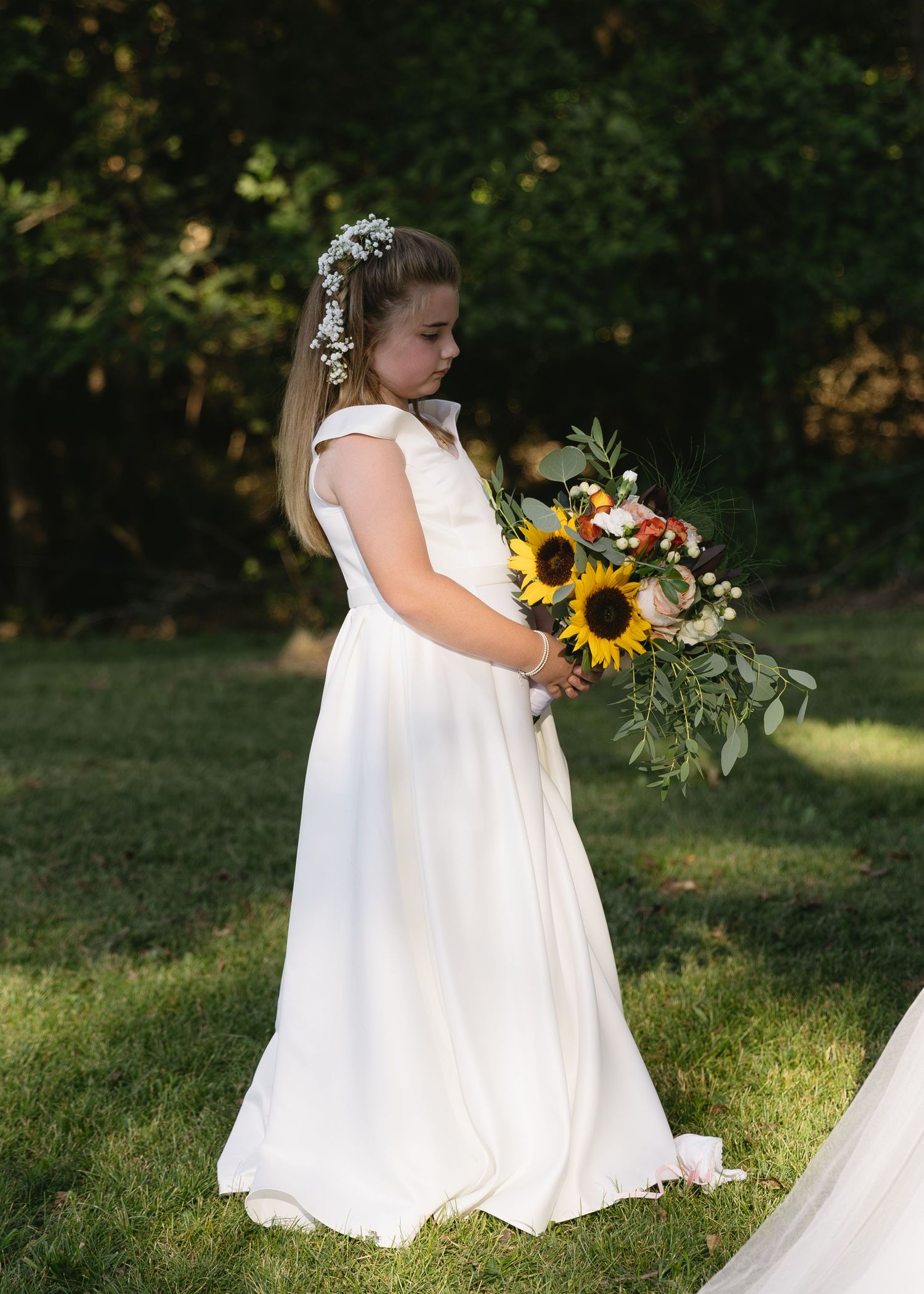 White wedding dress with sunflower bouquet photographed in garden setting.