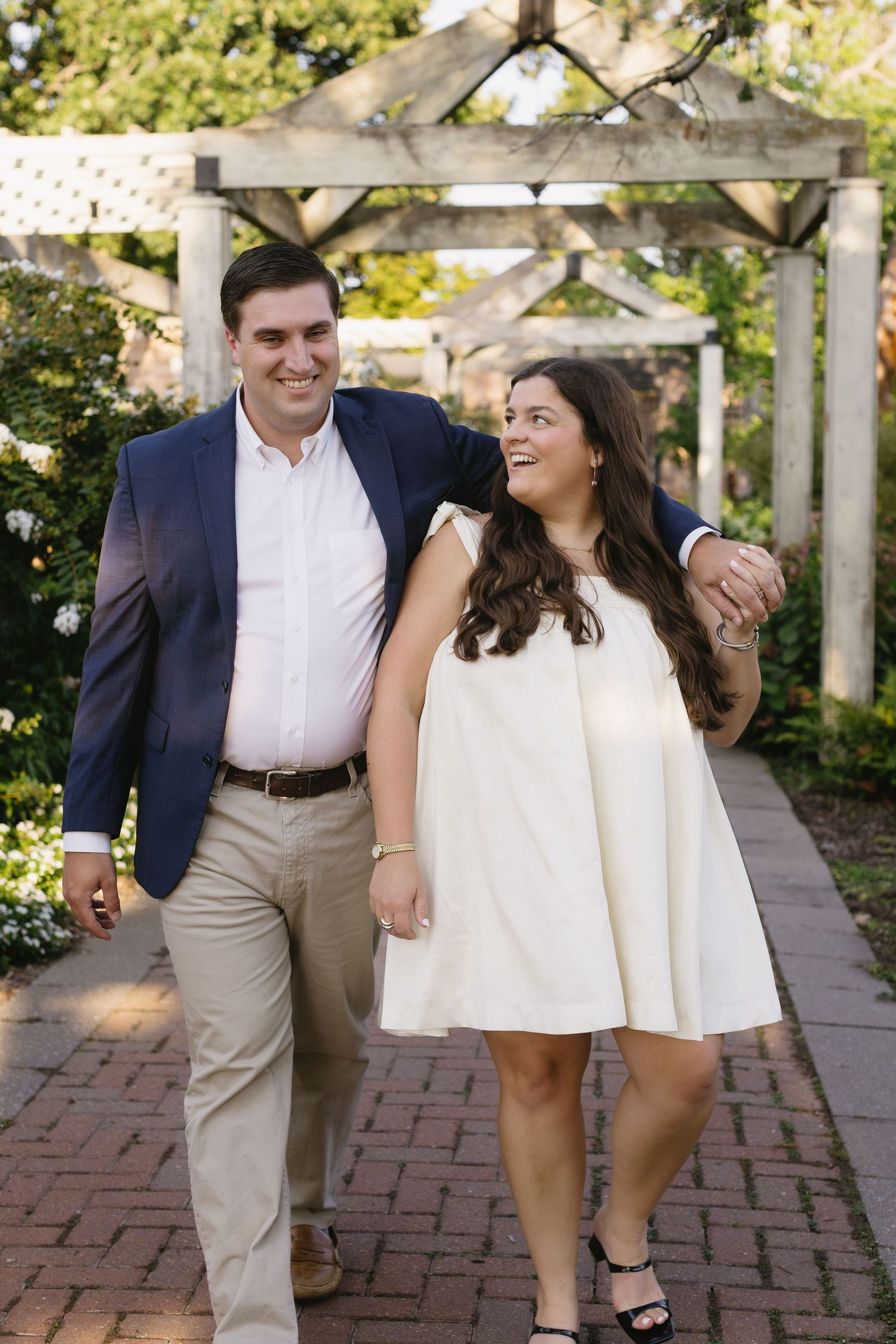 Couple shares romantic moments while walking along brick pathway in garden setting.