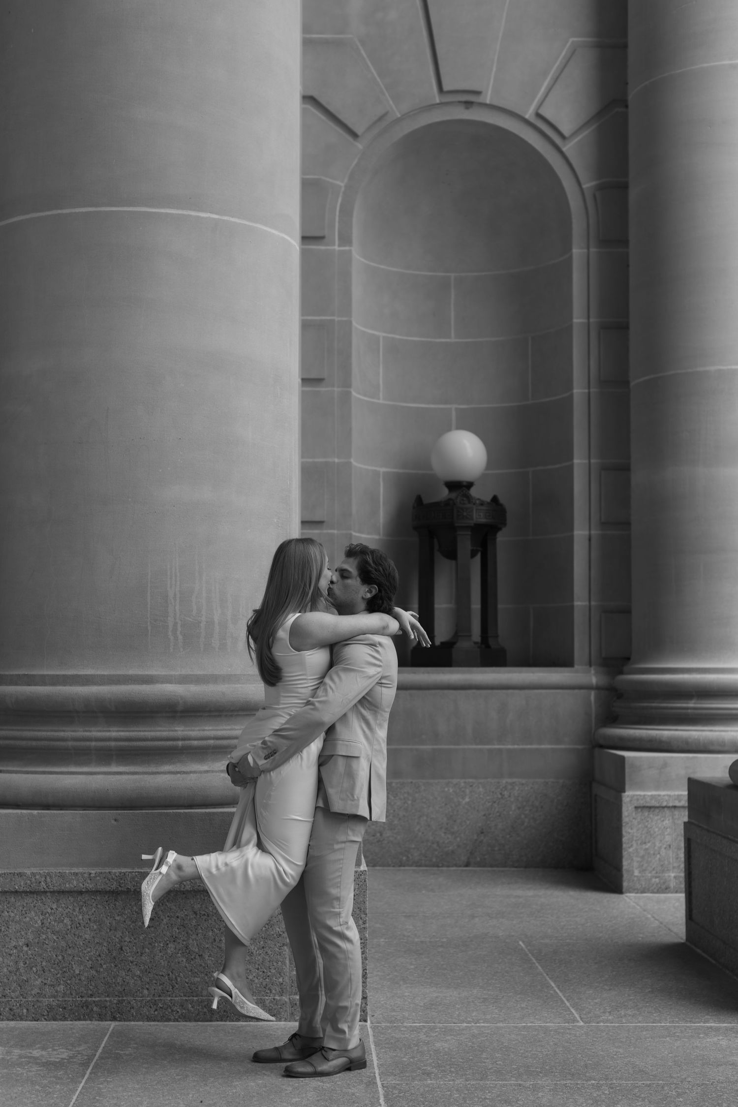 A romantic black and white photo of a couple embracing between classical columns.