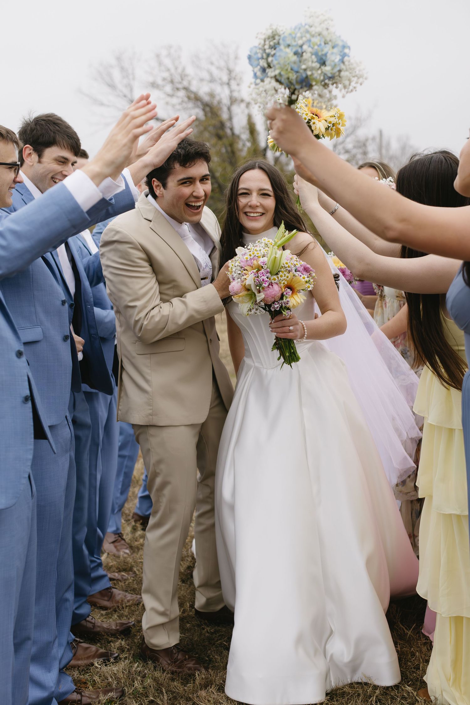 Wedding party forms celebratory arch tunnel with raised arms as couple walks through.