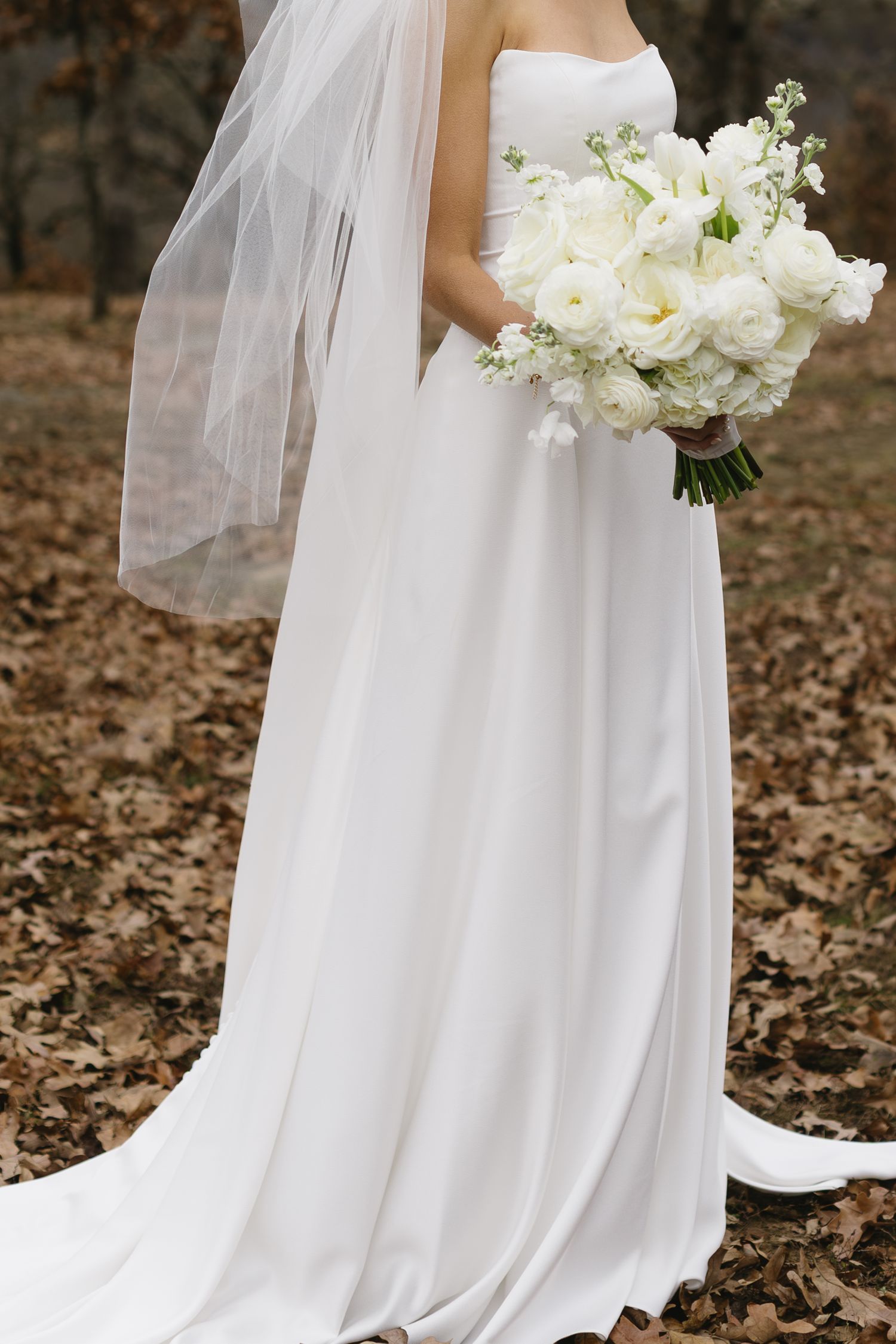 A detailed view of a white bridal bouquet against a flowing wedding dress.