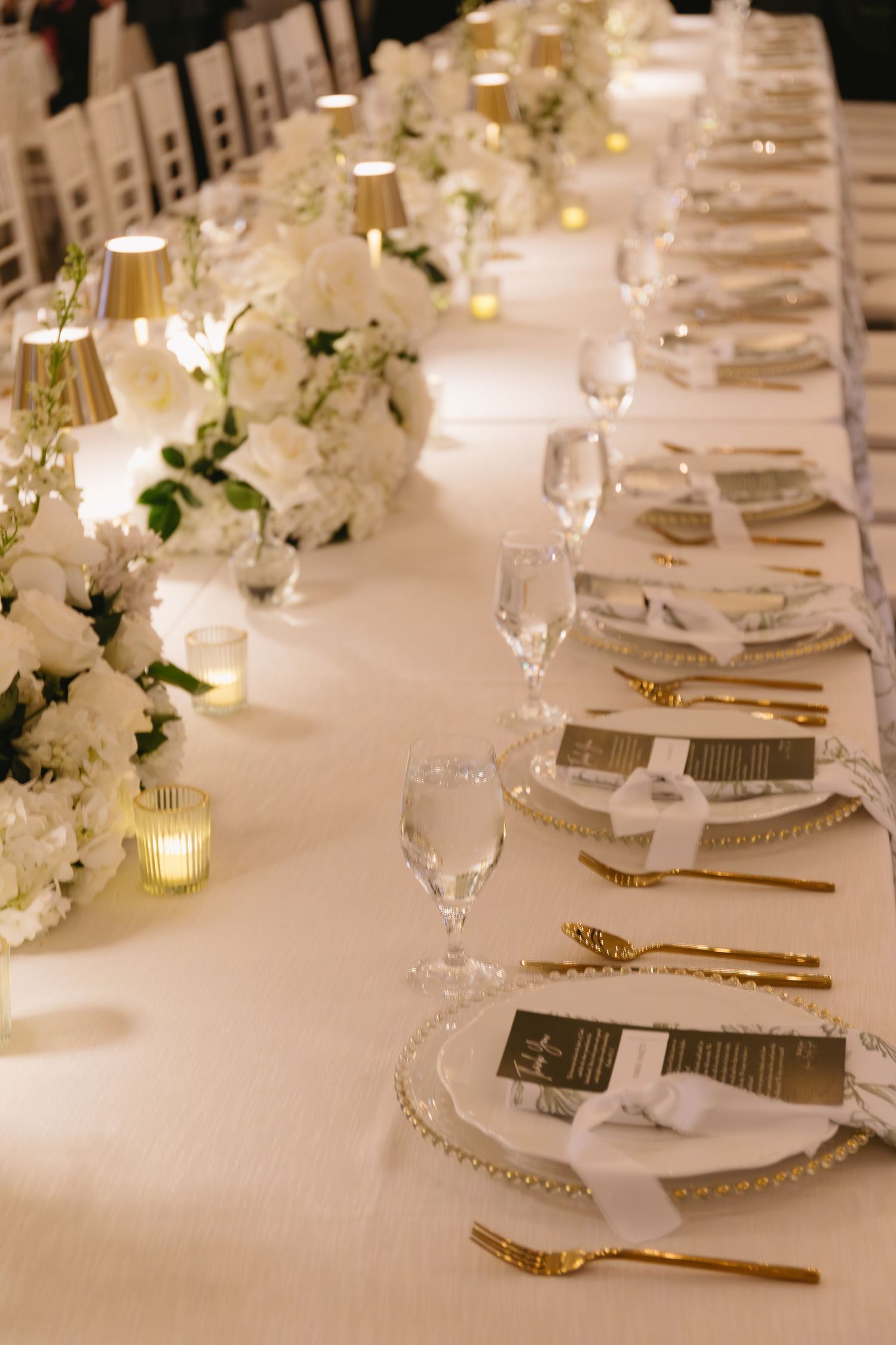 Elegant wedding table setting with white floral centerpieces and gold accents.