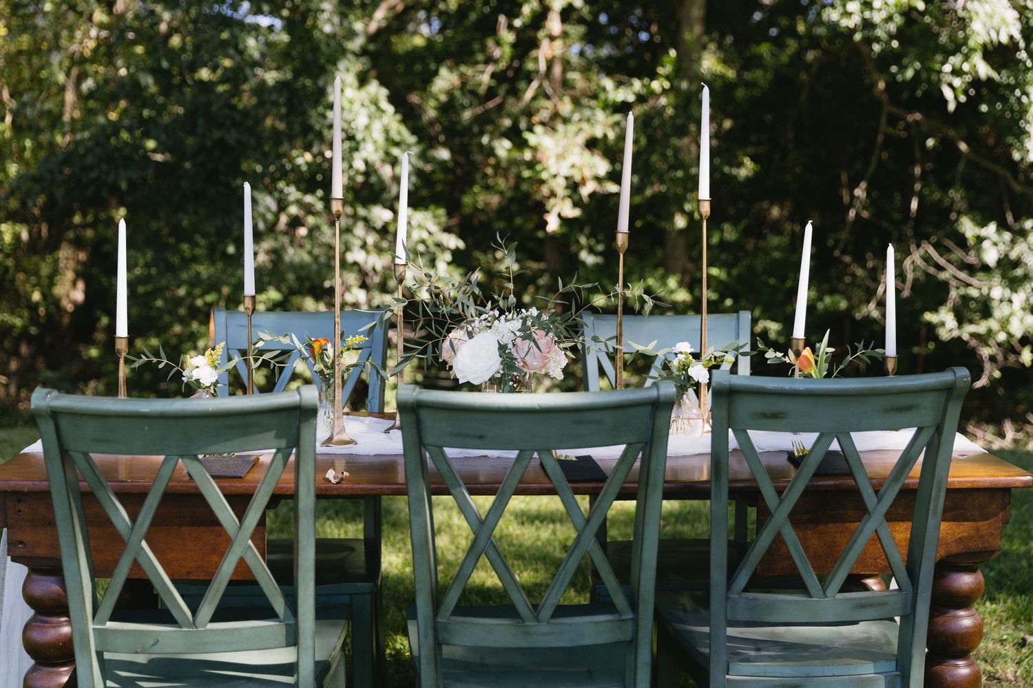 Row of sage green cross-back chairs set up for outdoor wedding ceremony.