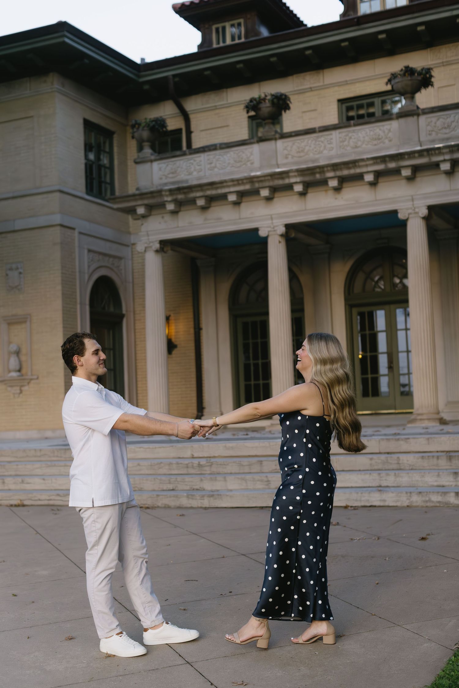 Couple playfully dances on outdoor patio near classical stone columns.
