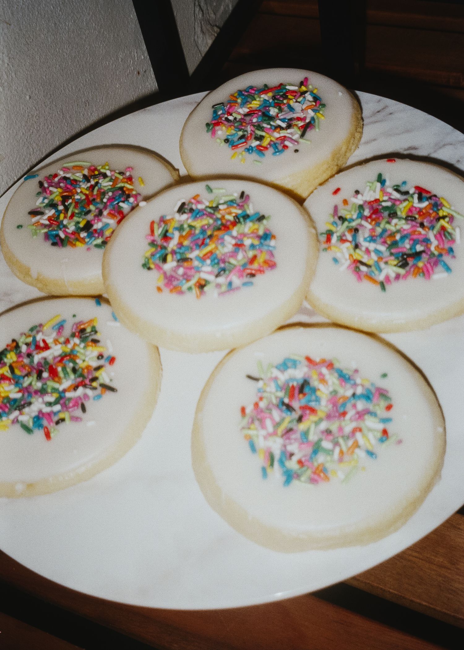 White frosted sugar cookies arranged on a plate with colorful rainbow sprinkles on top.