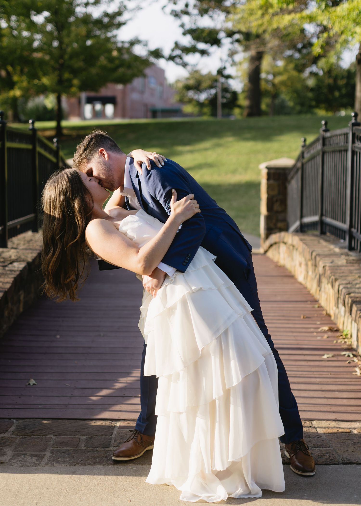 A romantic wedding couple shares a passionate dip kiss on an outdoor brick walkway.