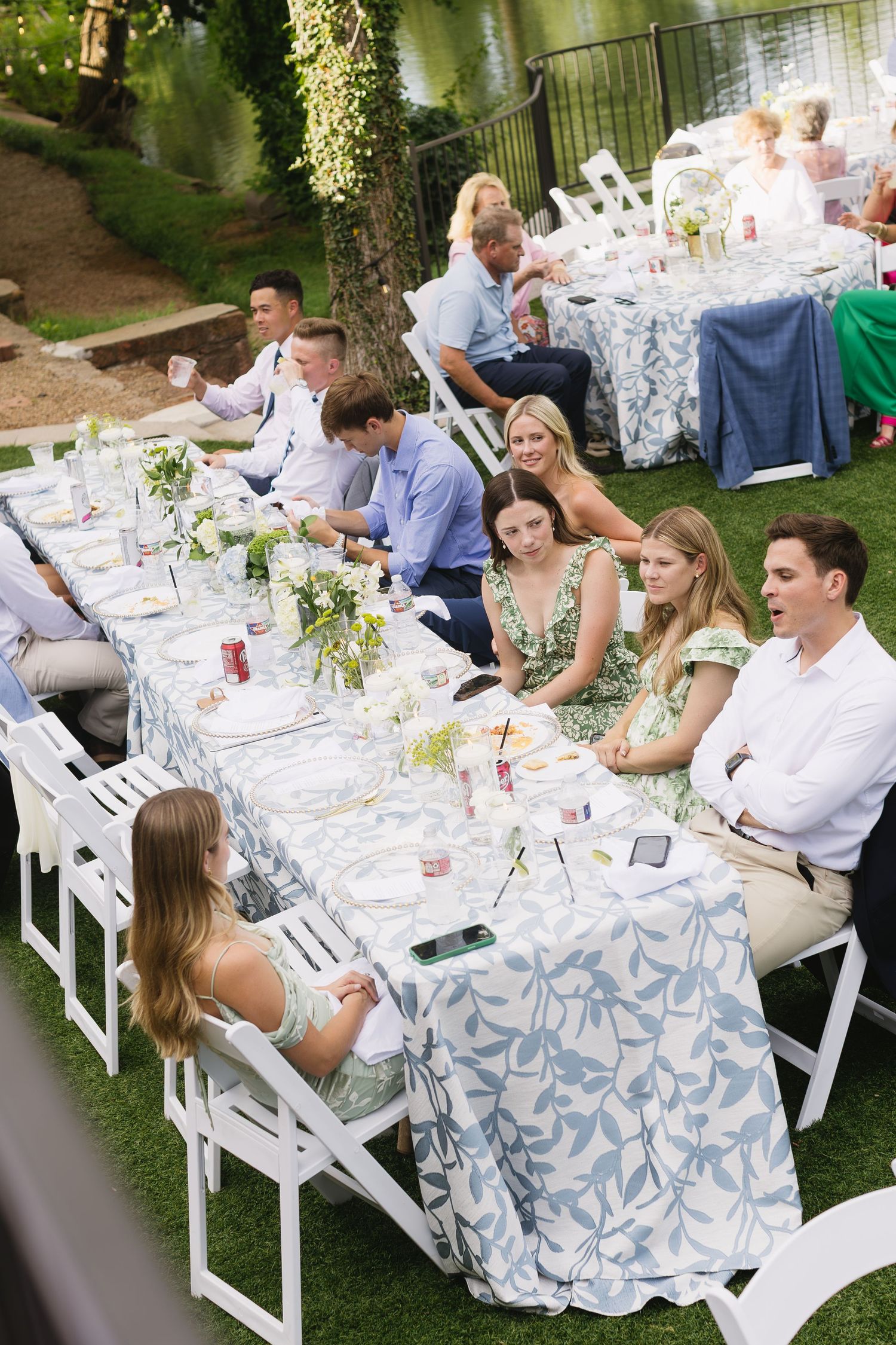 Wedding reception dinner tables set with white linens and floral centerpieces in an outdoor garden setting.