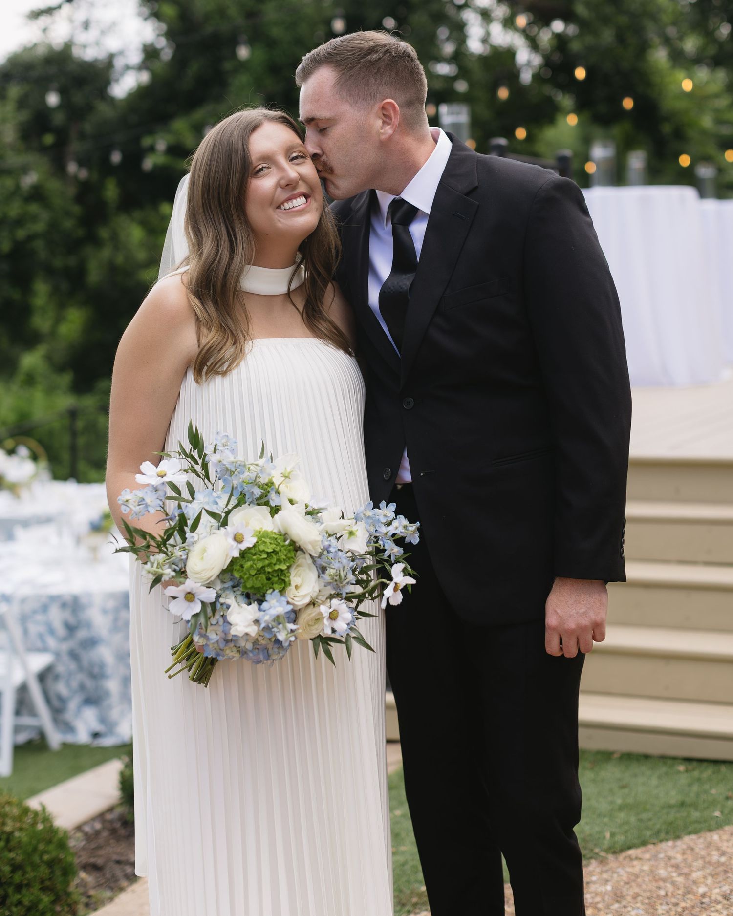 Wedding couple sharing intimate moment with bridal bouquet in outdoor garden setting.