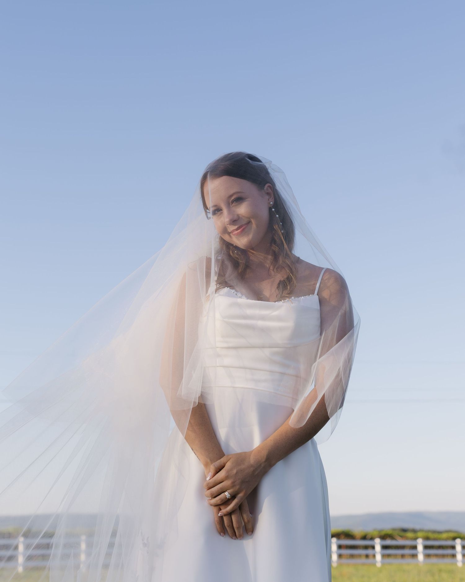 A candid bridal portrait showing natural laughter and joy against a rural backdrop.