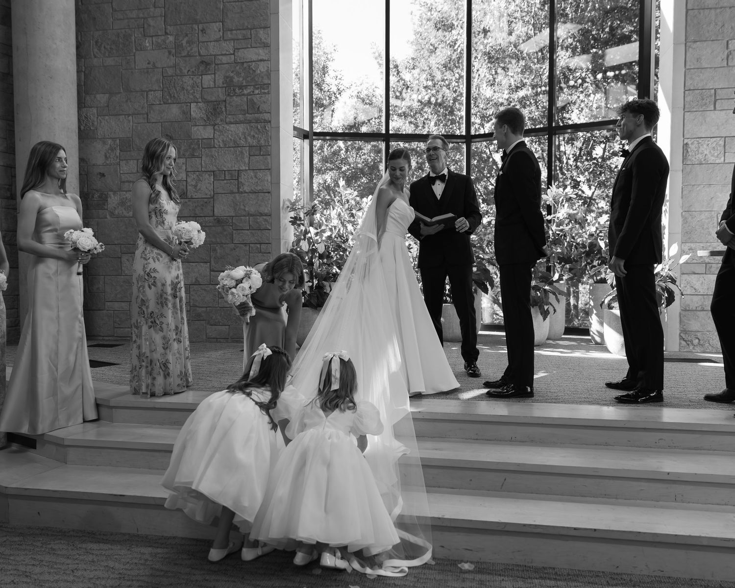 Wedding ceremony scene at a stone columned venue with bridal party and guests in attendance.