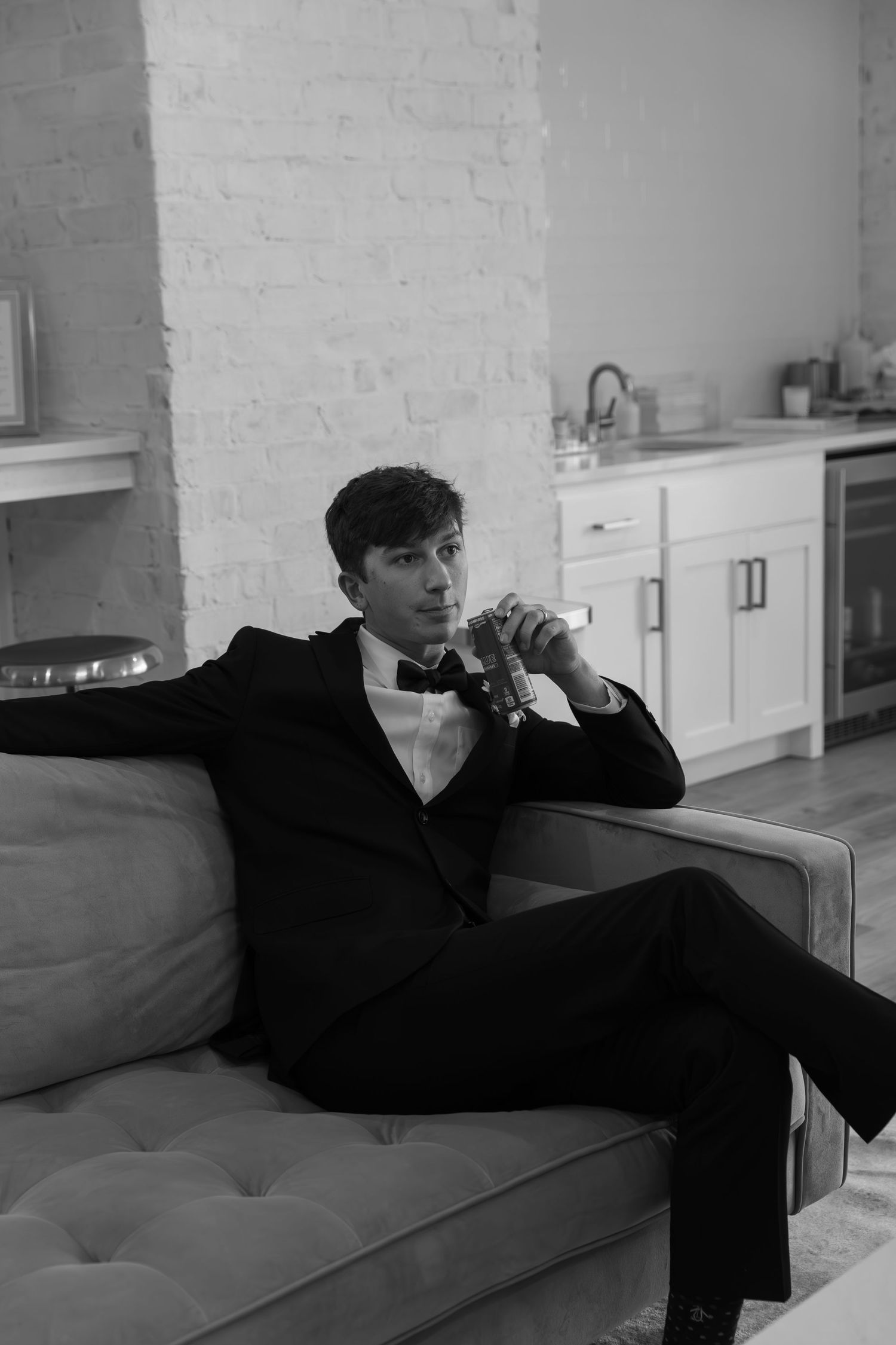 Black and white photo of someone lounging on a modern gray couch against a white brick wall.