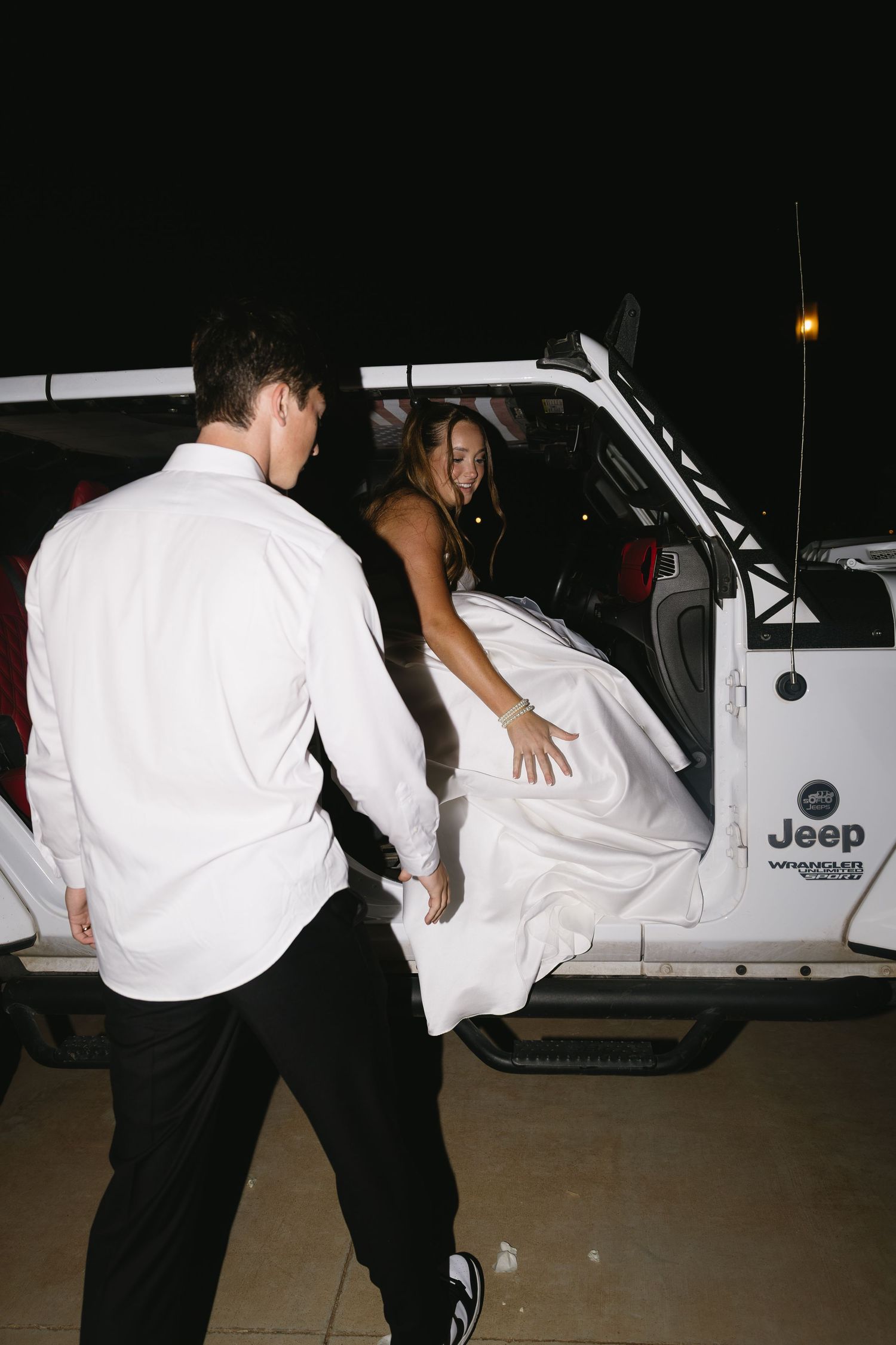Wedding couple getting into a white Jeep vehicle at night after their celebration.