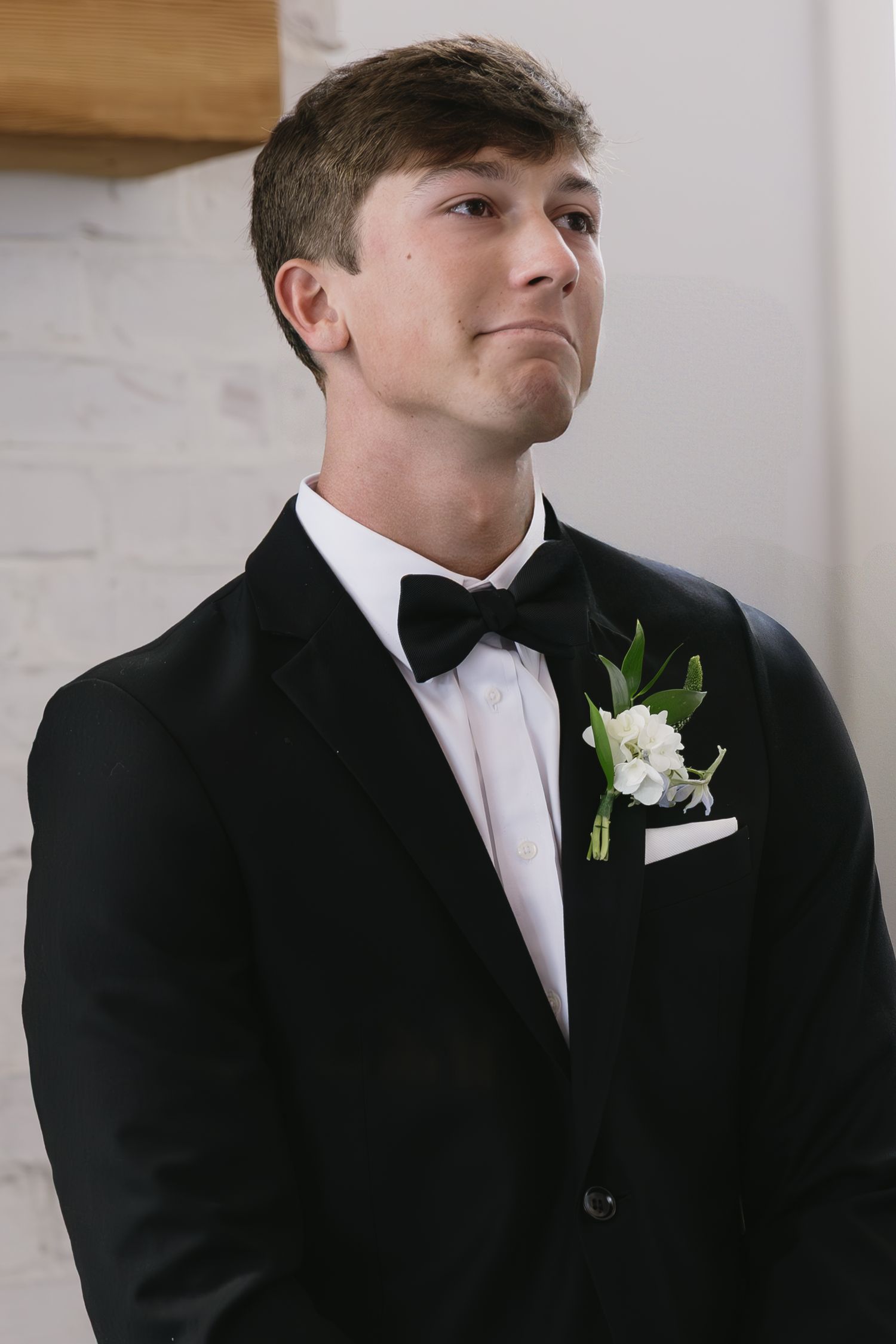 Groom in black tuxedo with white boutonniere shows various expressions in indoor portraits.