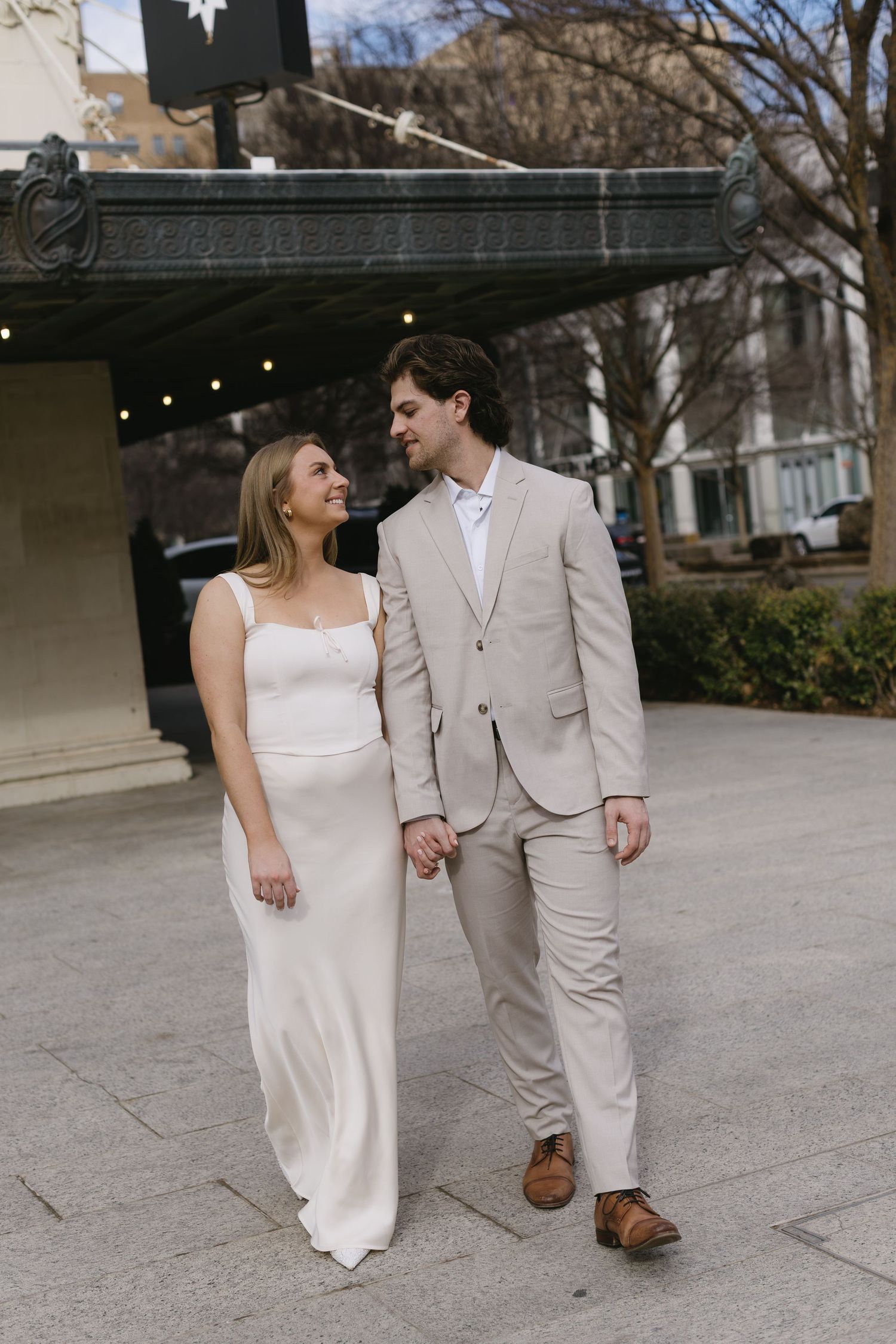 Couple in coordinated formal wear walks together on an outdoor plaza.