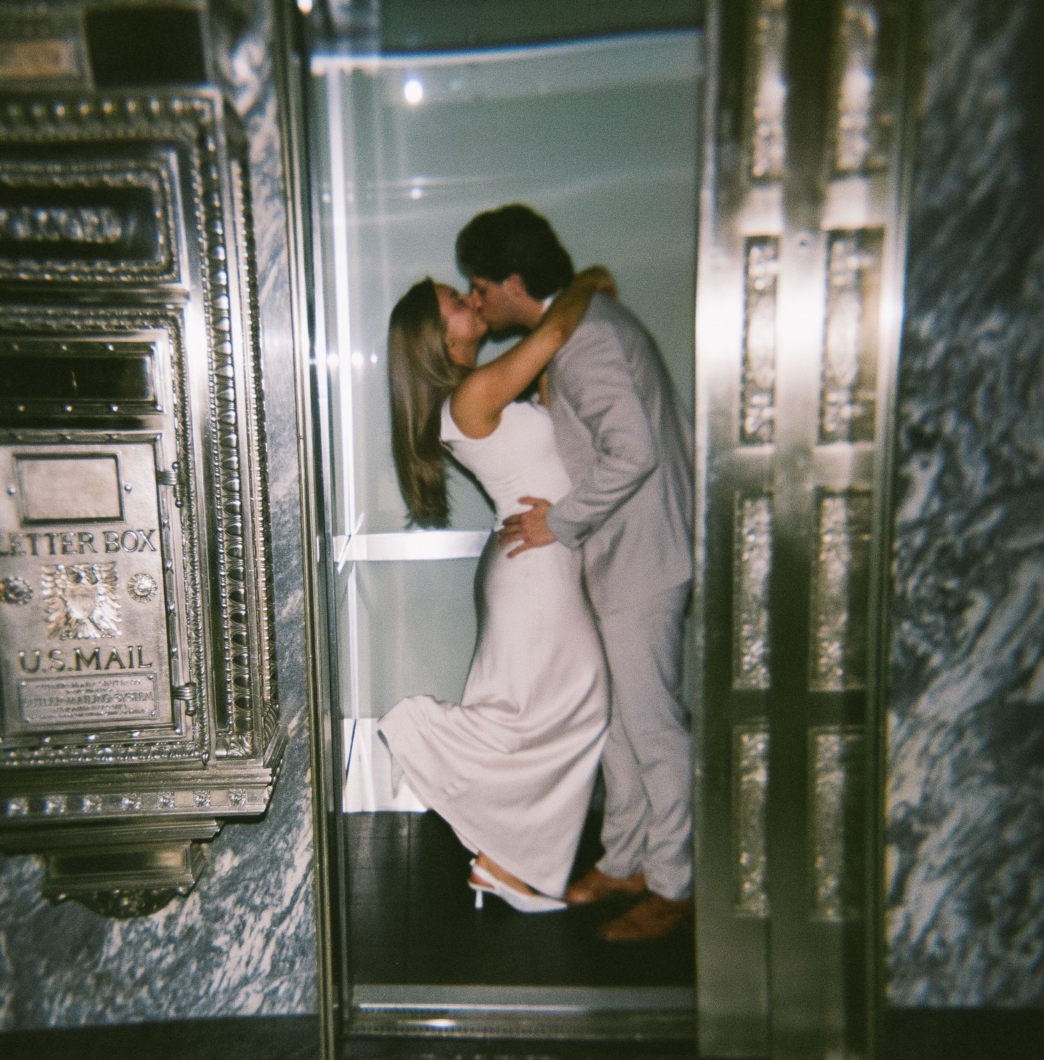 A romantic couple in formal wear share an intimate kiss in an elegant elevator.