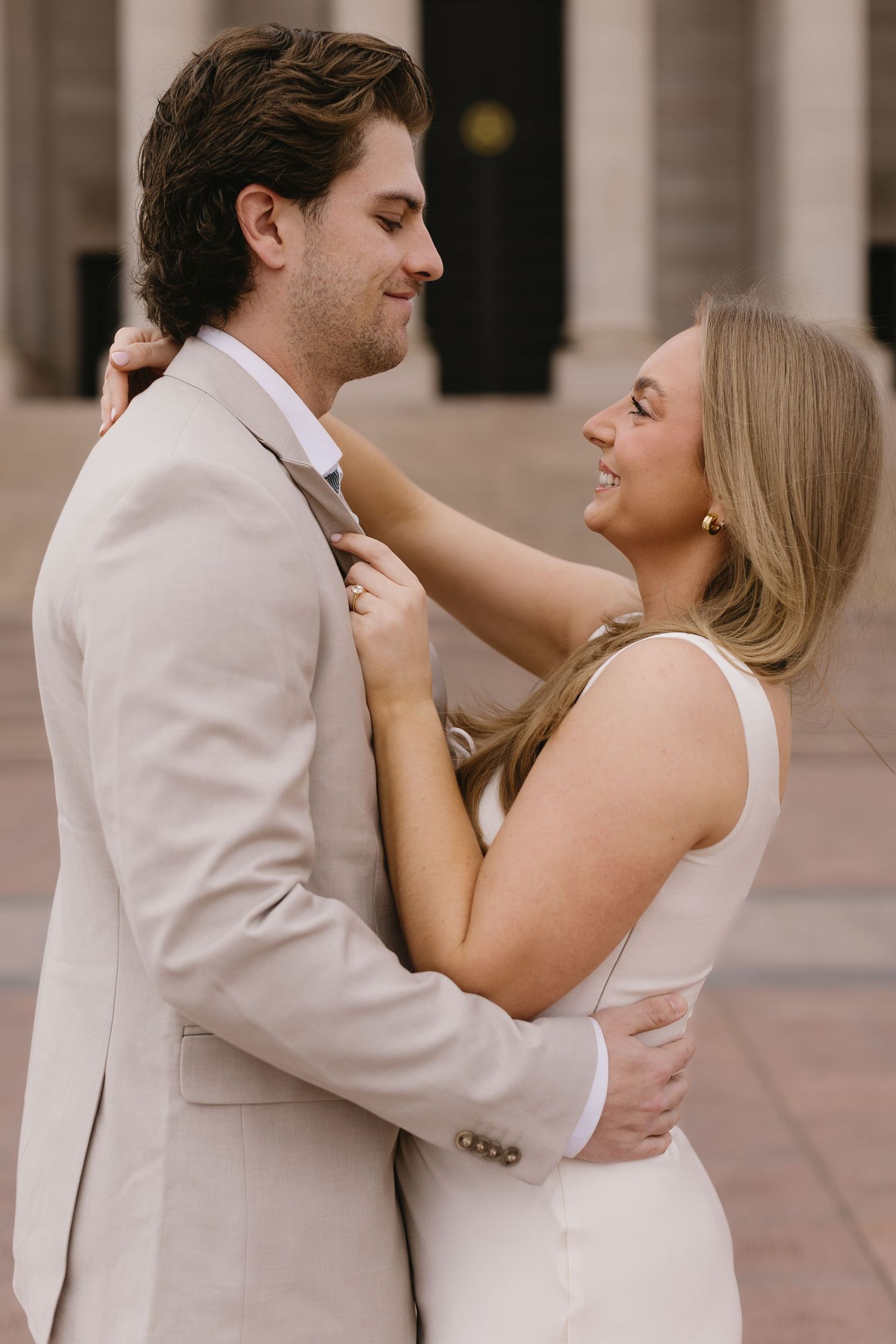A romantic moment between a couple in formal wear embracing in front of classical architecture.