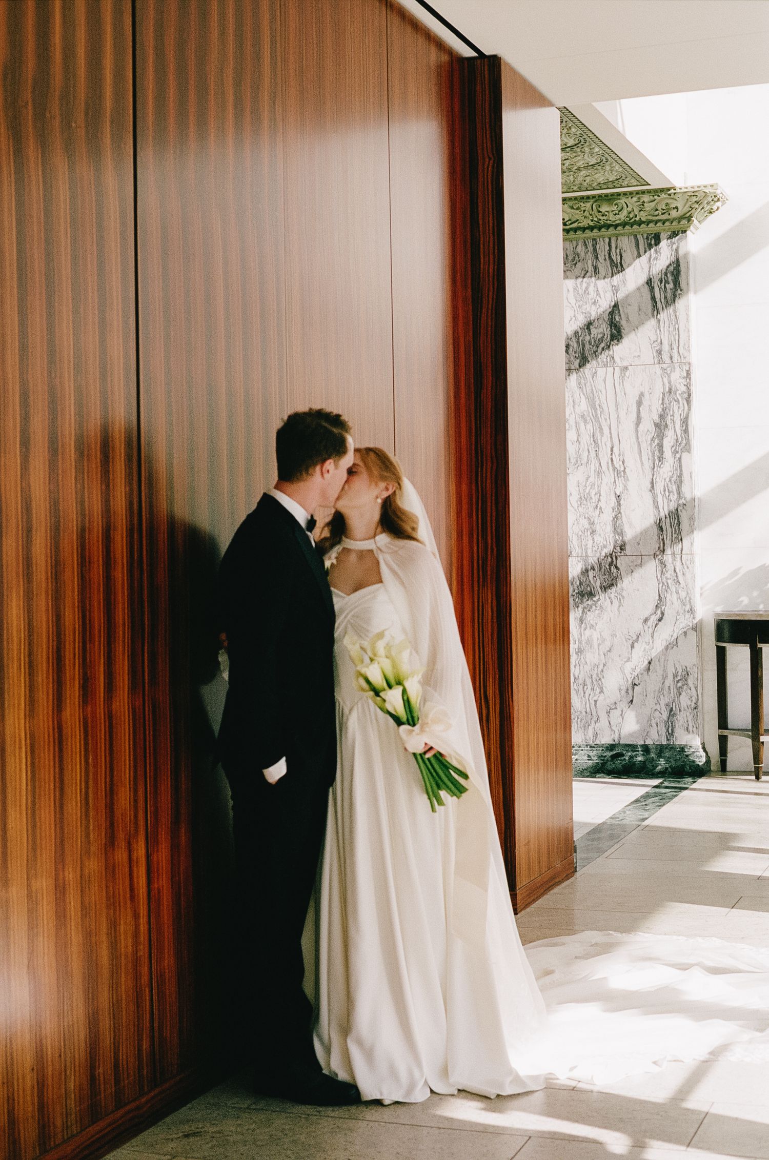 Wedding couple shares a moment against wooden paneled walls in natural lighting.