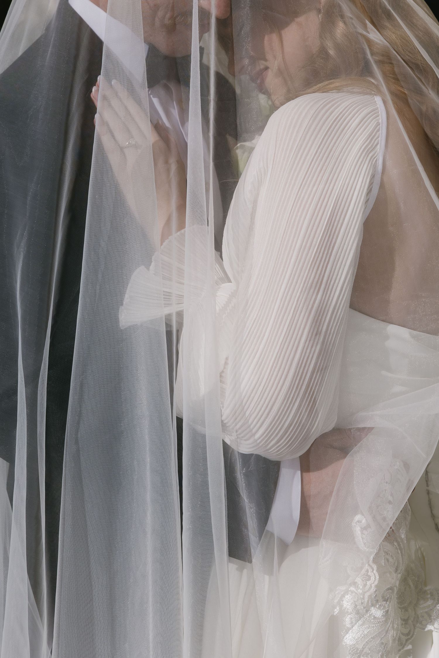 Close-up details of pleated wedding dress bodice through sheer veil.