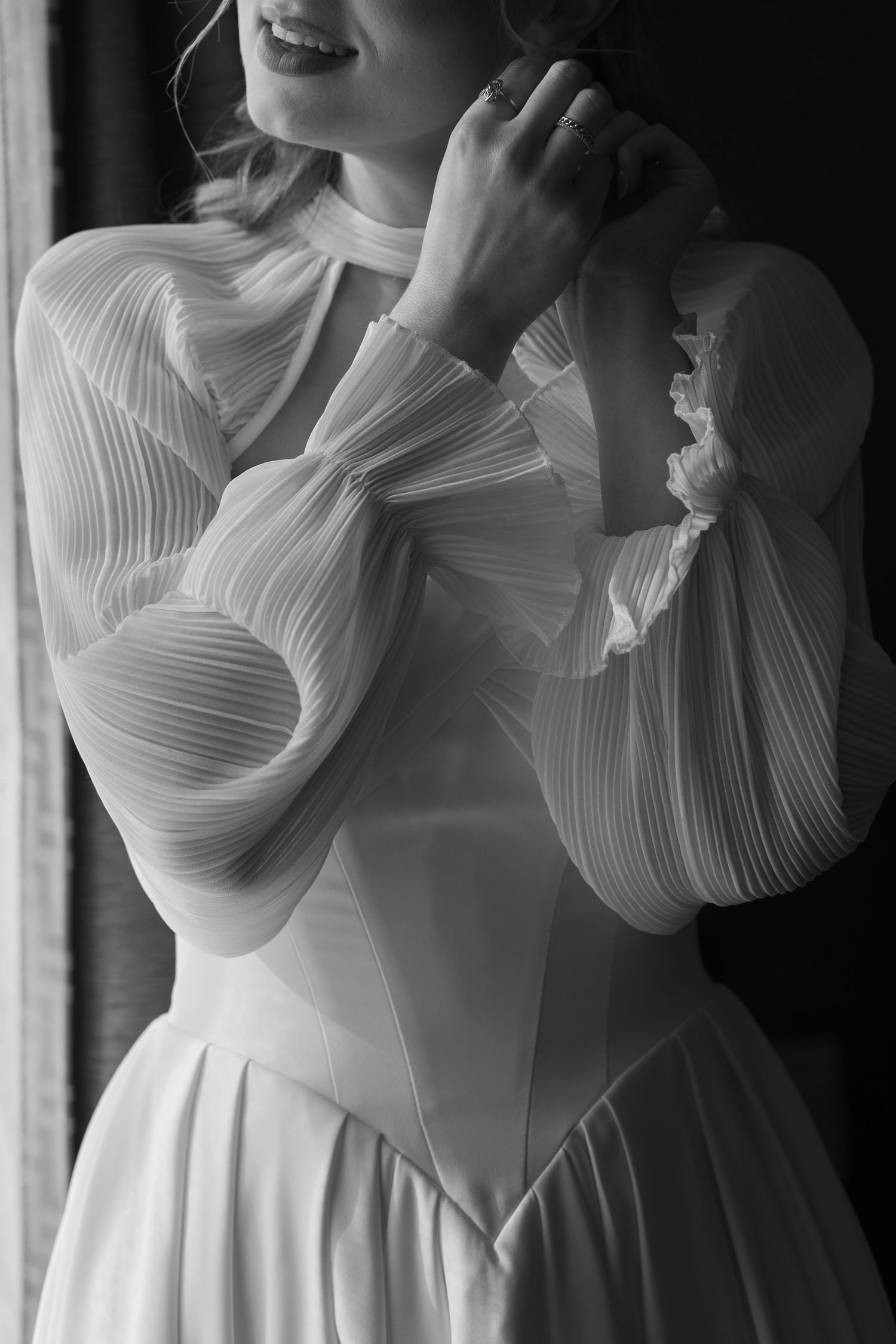 Close-up details of a white wedding dress showing intricate pleated fabric and dramatic sleeves.