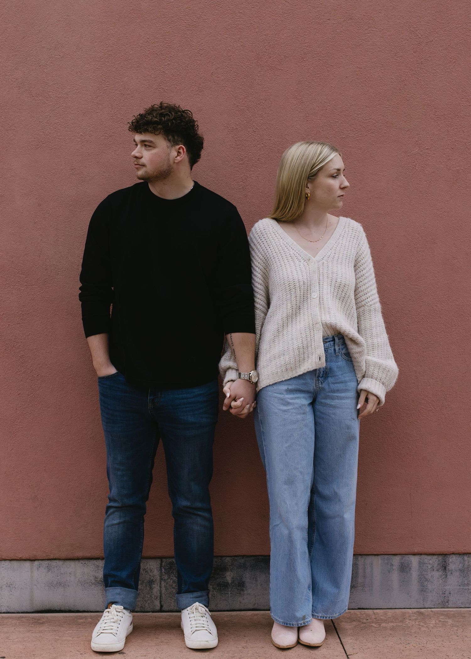 Couple in casual outfits posing against a terracotta colored wall.