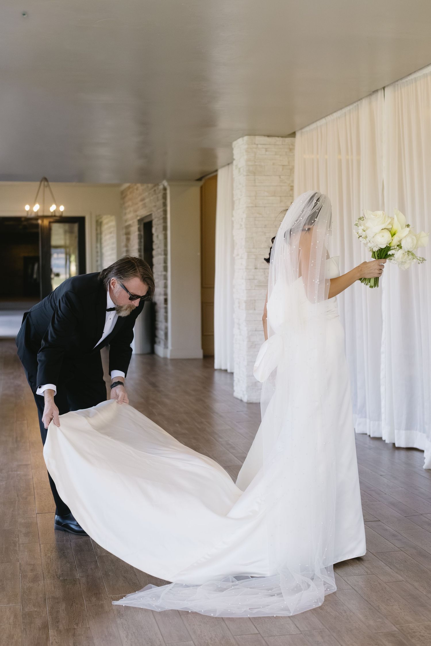 Helper arranging the train of a bride's flowing white wedding gown.