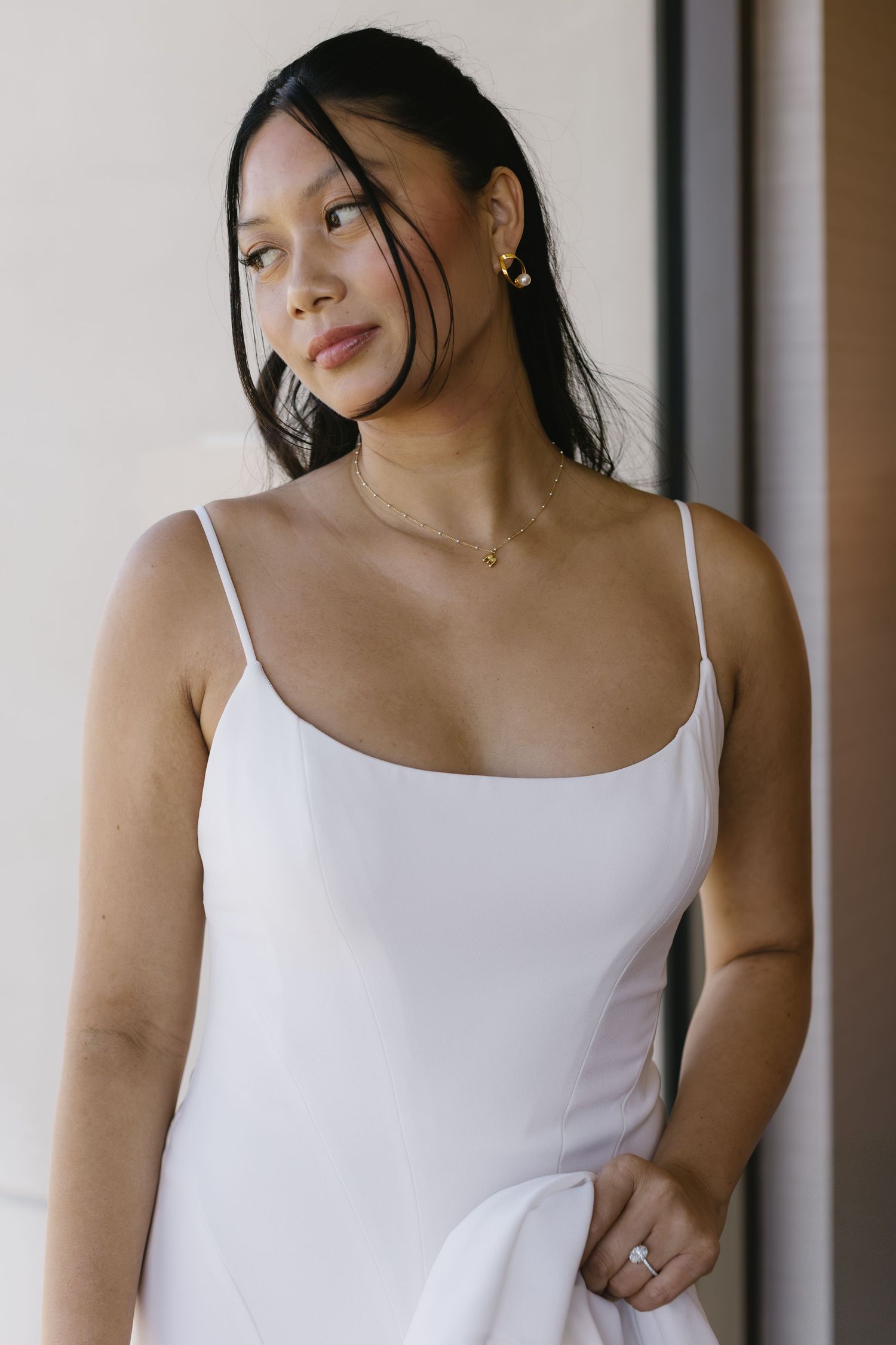 Bride wearing a simple white spaghetti strap dress poses against a neutral background.