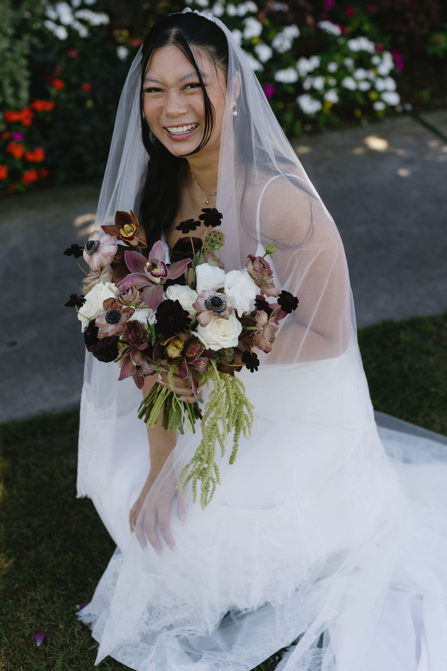 Bride in a white wedding dress holds a stunning bouquet of white and purple flowers.