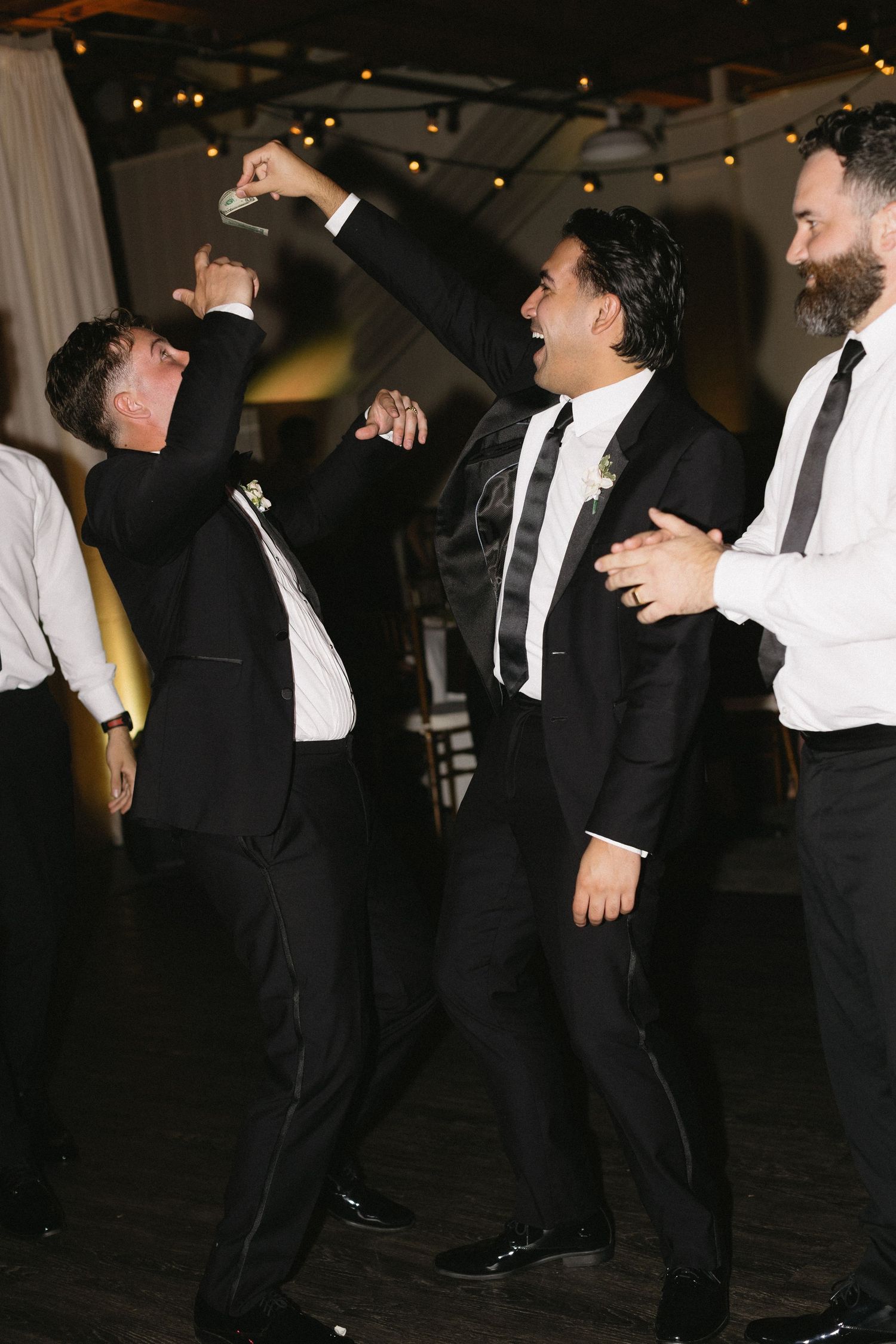 Wedding guests dance and celebrate in formal attire under indoor lighting.