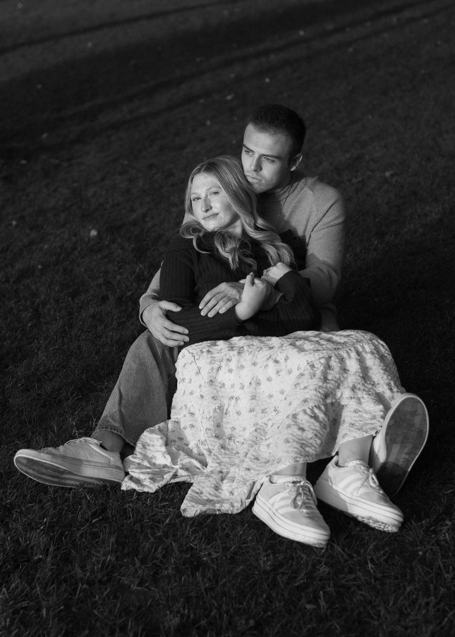A couple relaxes together on grass during a black and white photoshoot.