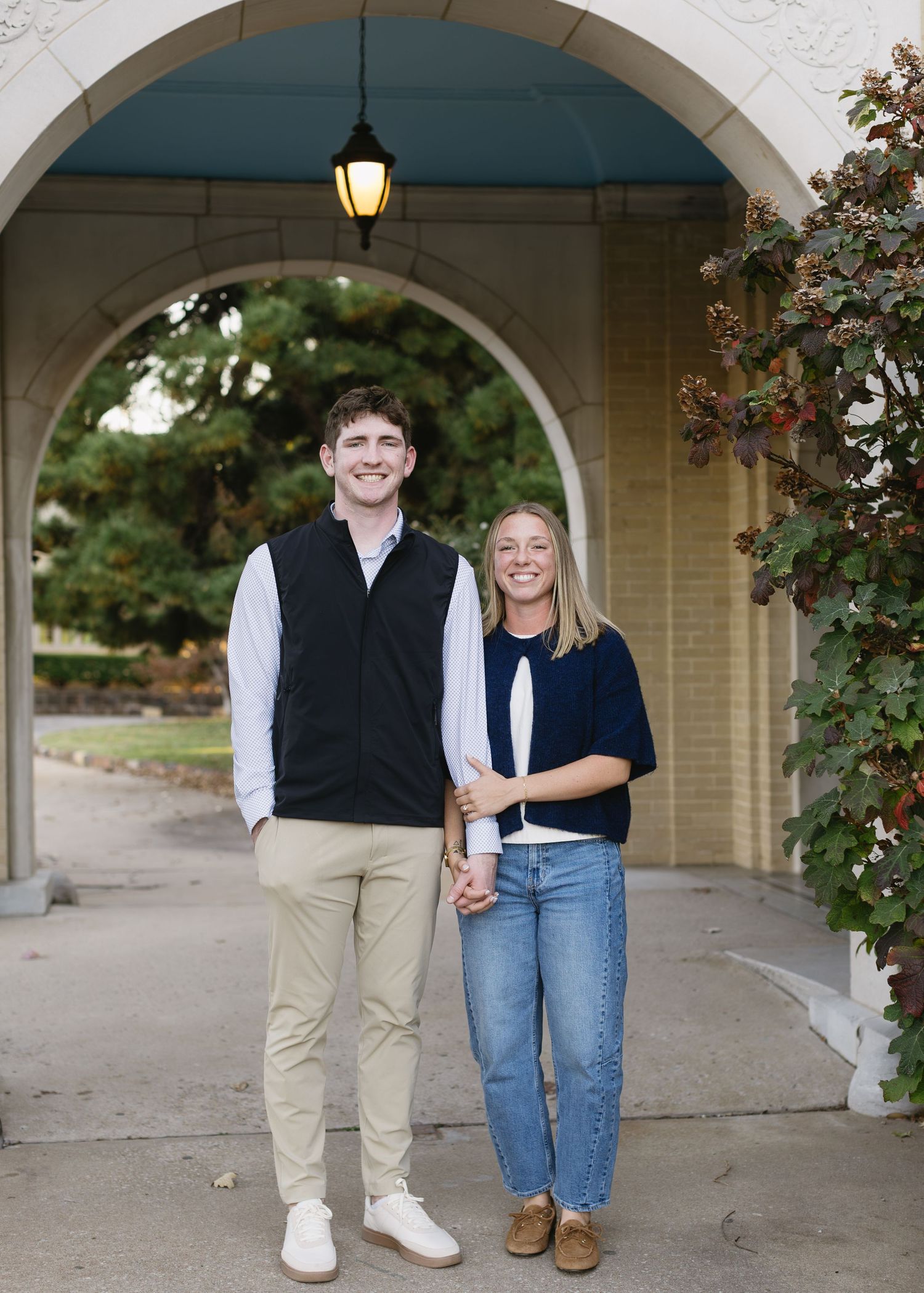 A couple shares candid moments while walking through an outdoor archway corridor in casual attire.