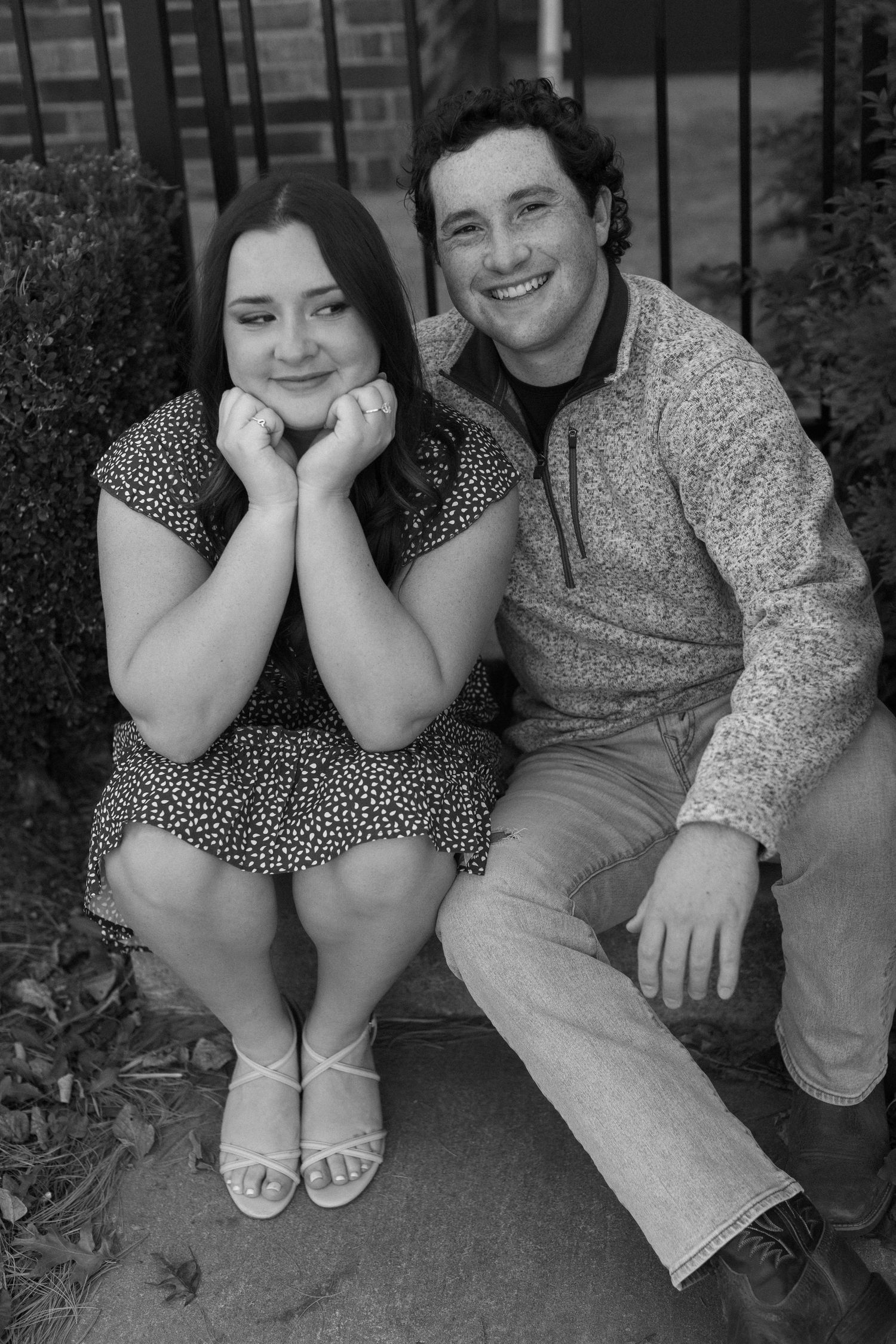 A couple sits close together on outdoor steps during a casual engagement photoshoot.