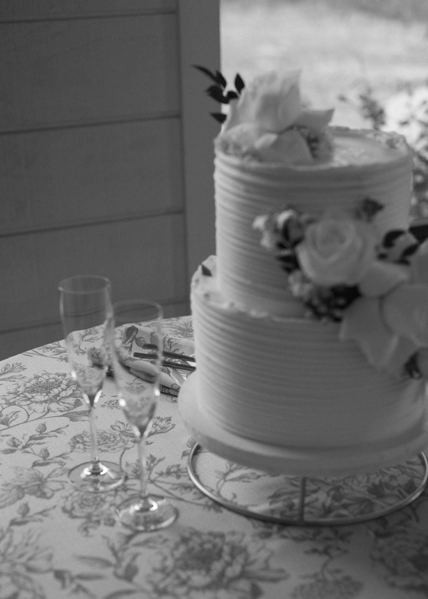 An elegant white wedding cake with floral decorations sits on a lace-covered table.
